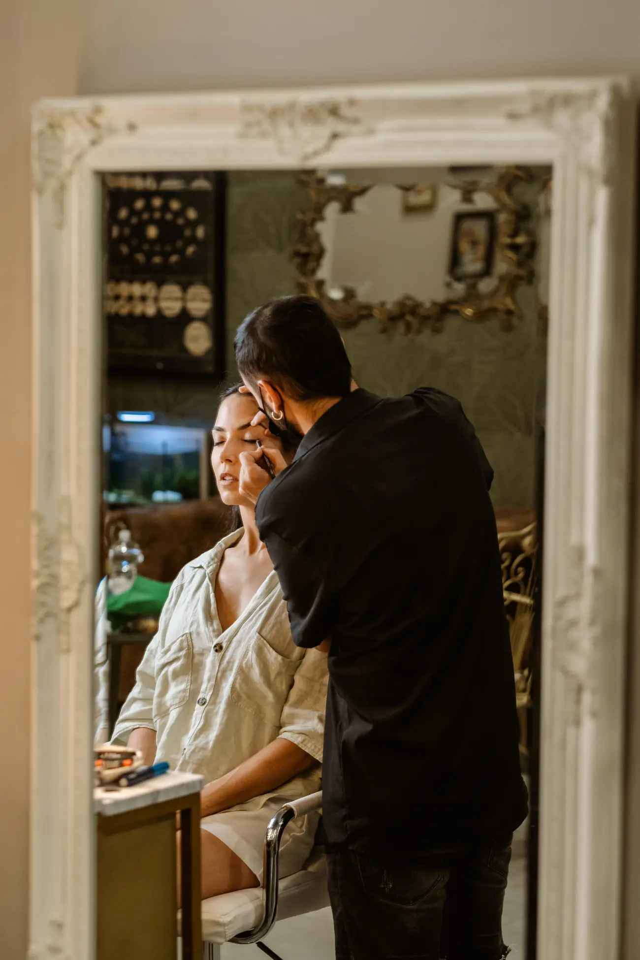 El maquillador prepara a la novia, reflejada en un espejo blanco, en Mérida