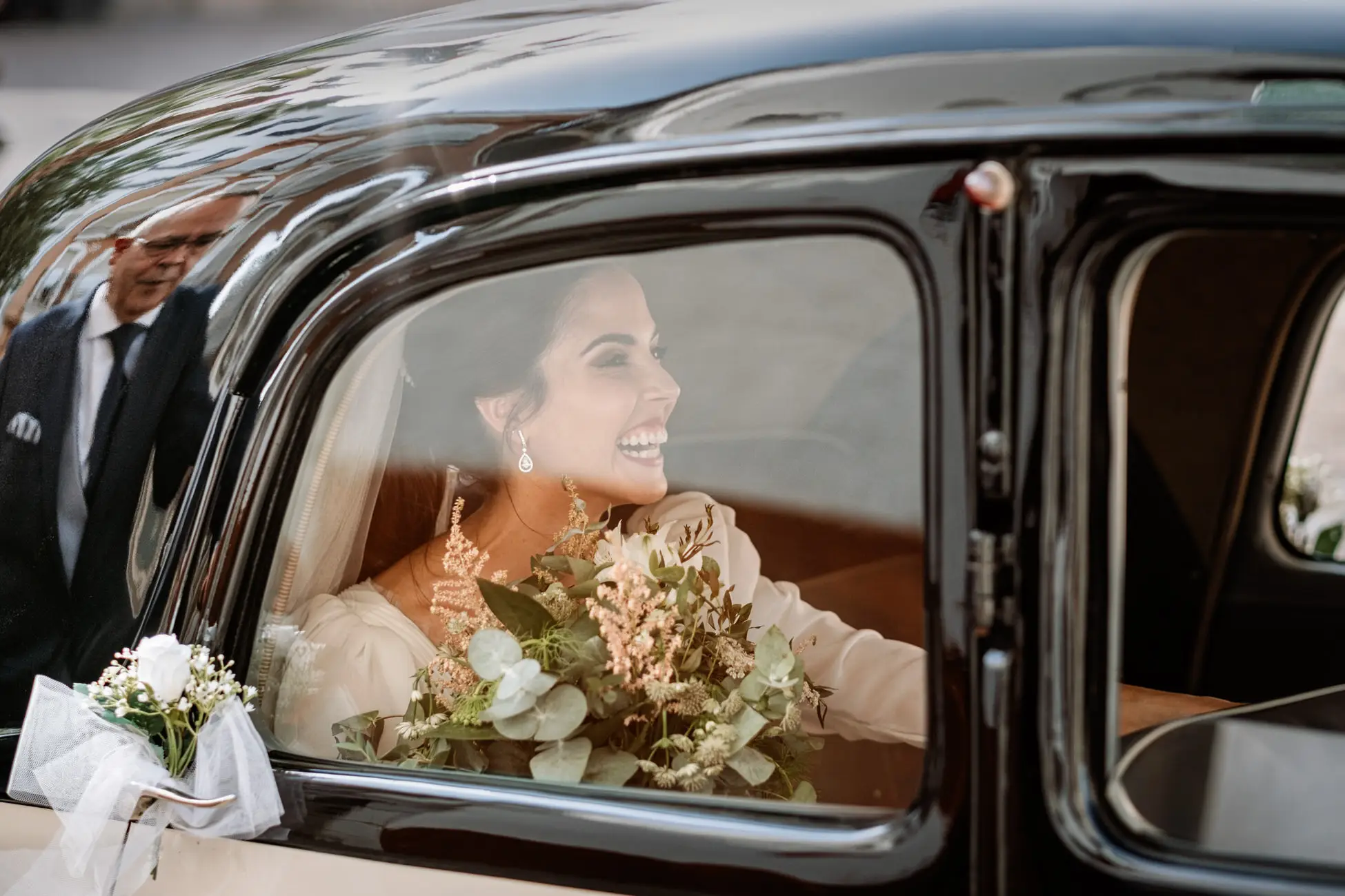 La novia sonríe dentro del coche clásico negro, en Mérida