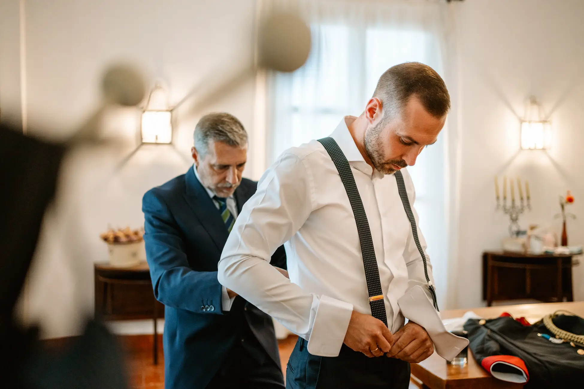 El novio se cambia el uniforme por el traje con ayuda de un familiar, en Mérida