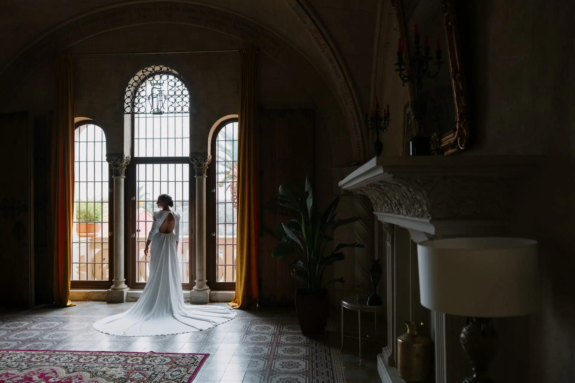 La novia de espaldas en un salón con ventanales arqueados