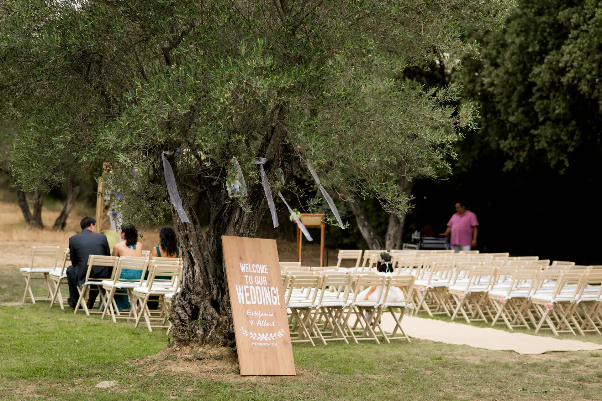 Sillas de la ceremonia entre olivos con cartel de bienvenida, en el Castell d'Empordà, Girona