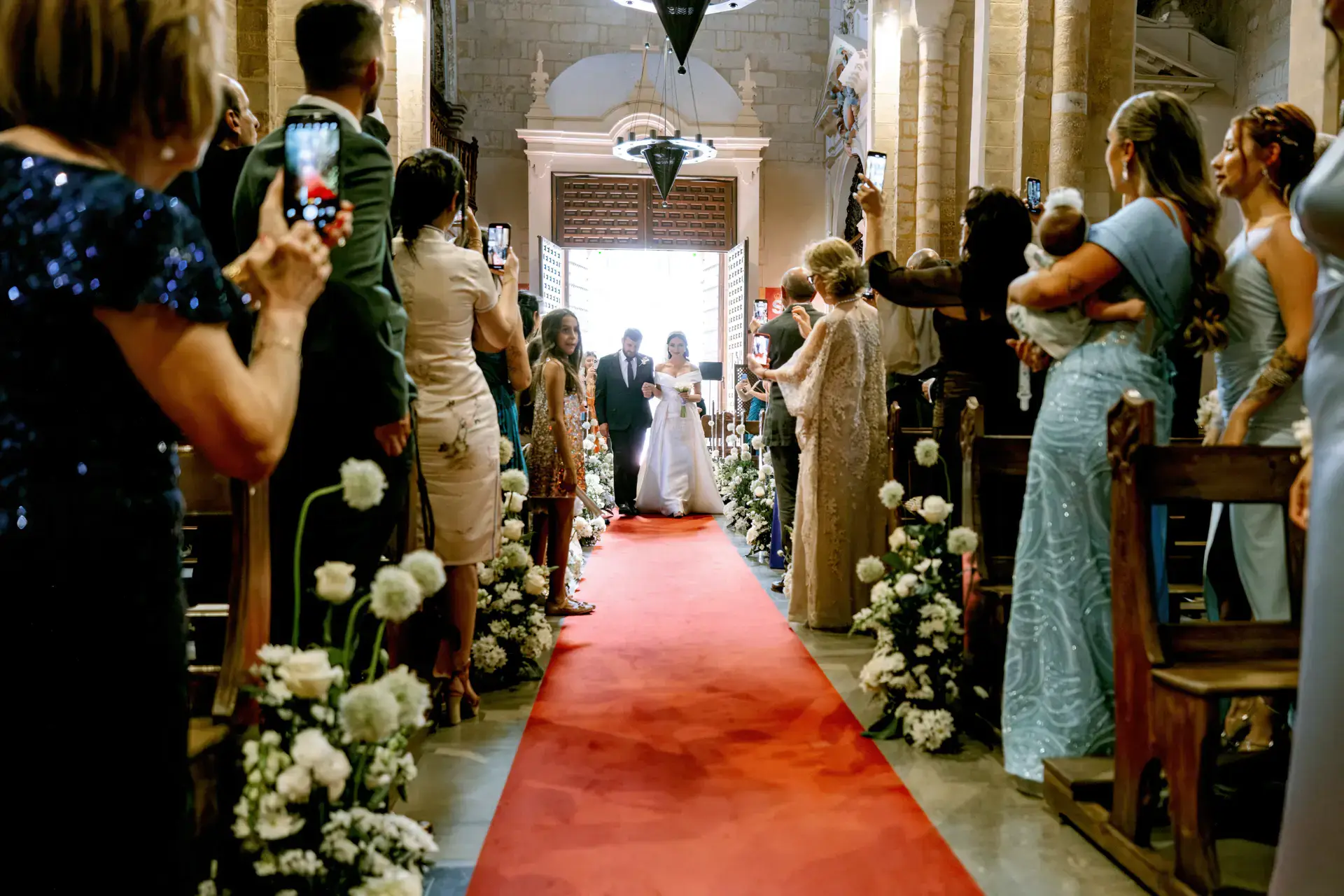 Nicole entra en la iglesia por la alfombra roja entre flores blancas, en Córdoba