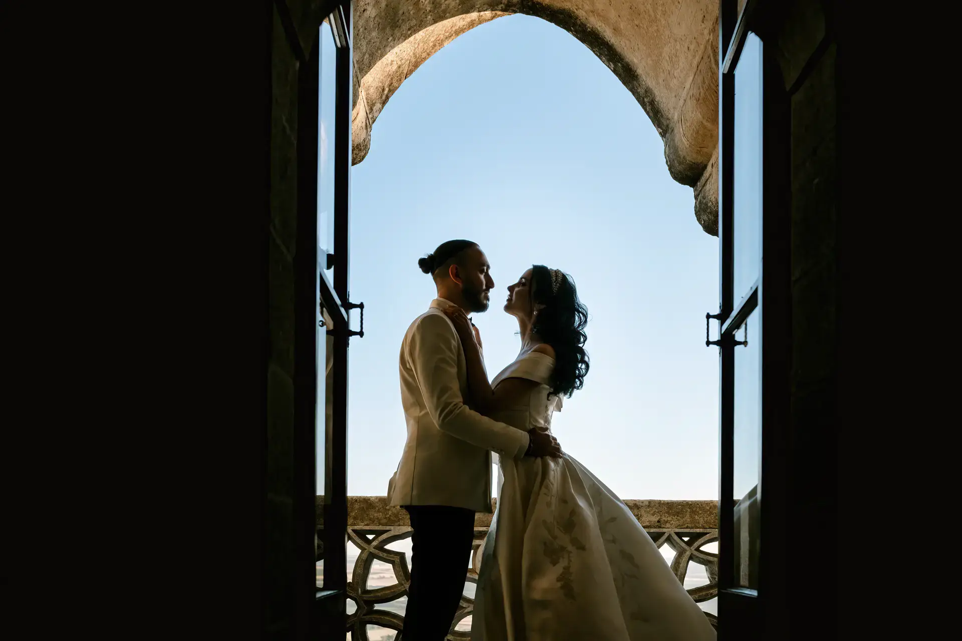 Nicole y Haytham a contraluz bajo un arco del castillo