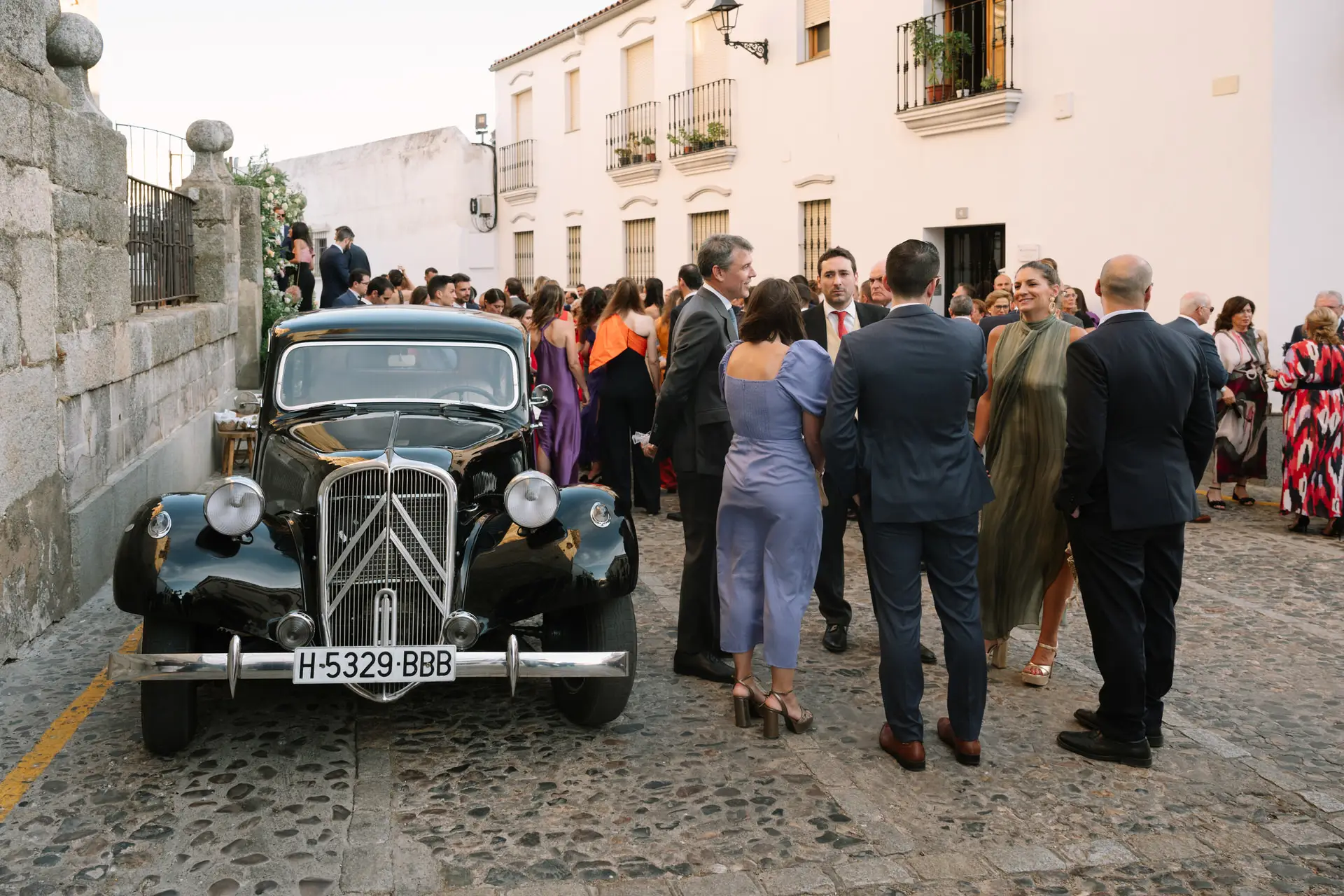 Invitados esperan a los novios junto al coche clásico en la calle, en Jerez de los Caballeros
