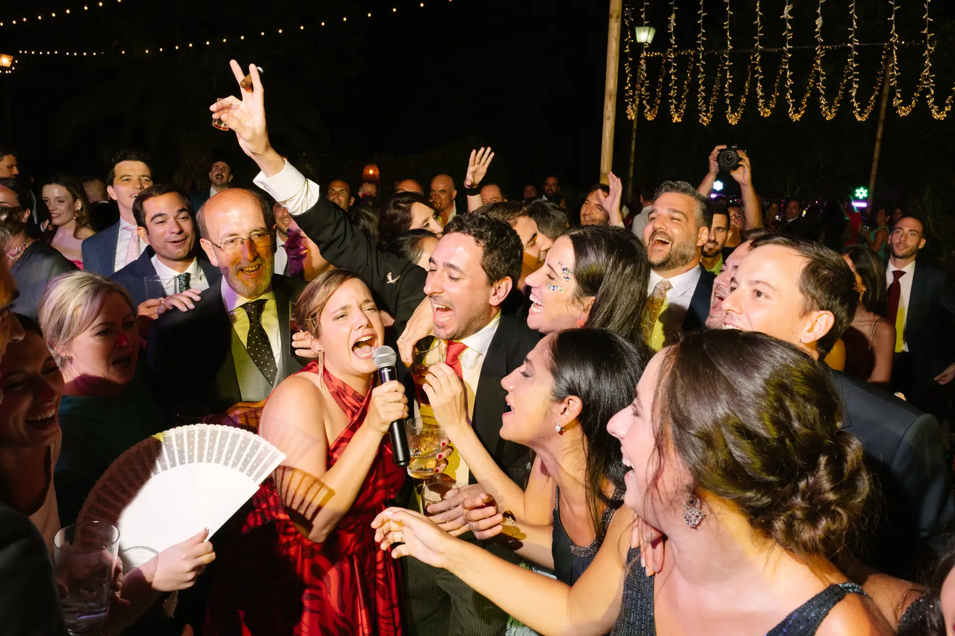 Una invitada canta con micrófono rodeada de amigos con abanicos, en Jerez de los Caballeros