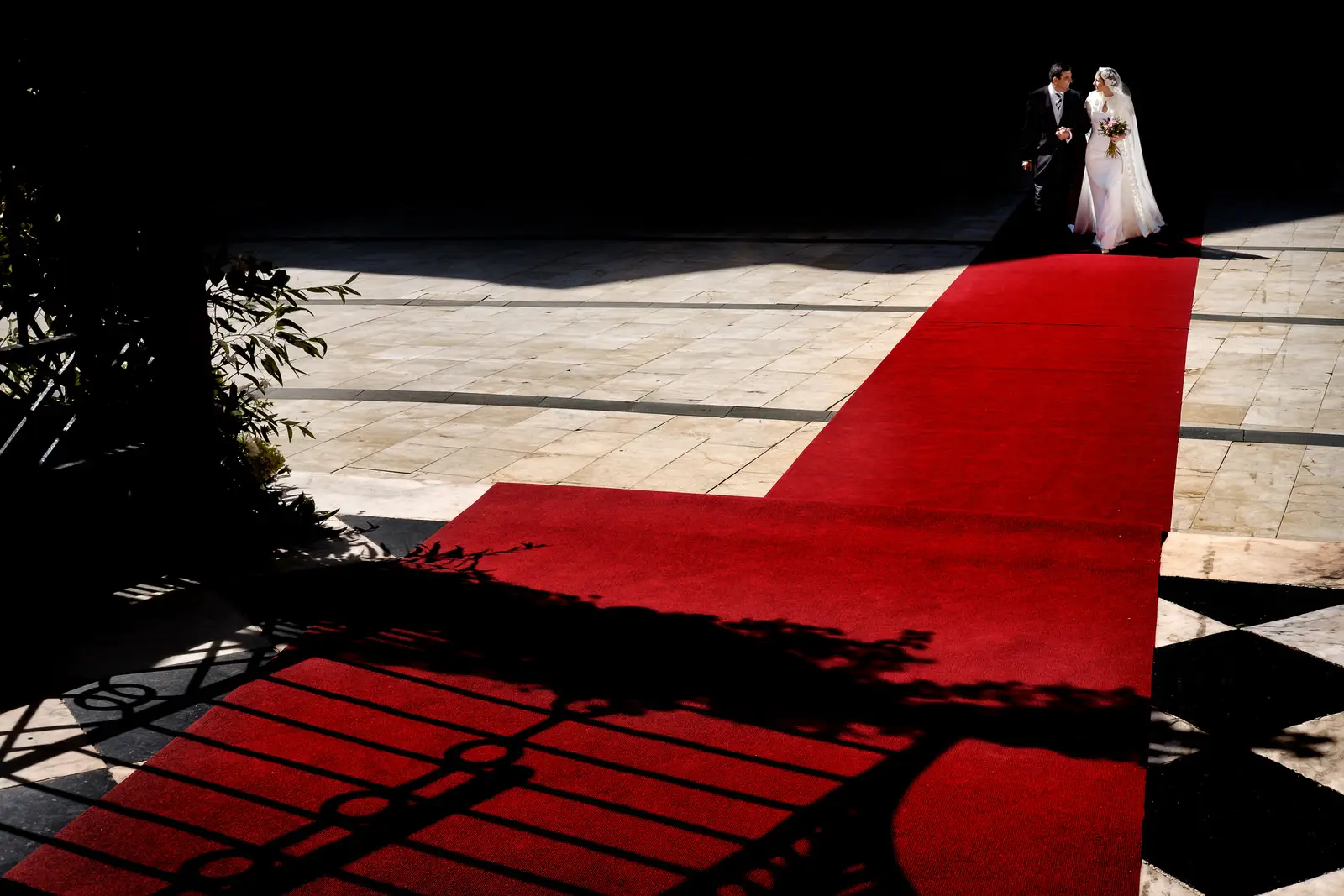 Los novios al final de una alfombra roja junto a la sombra de una reja