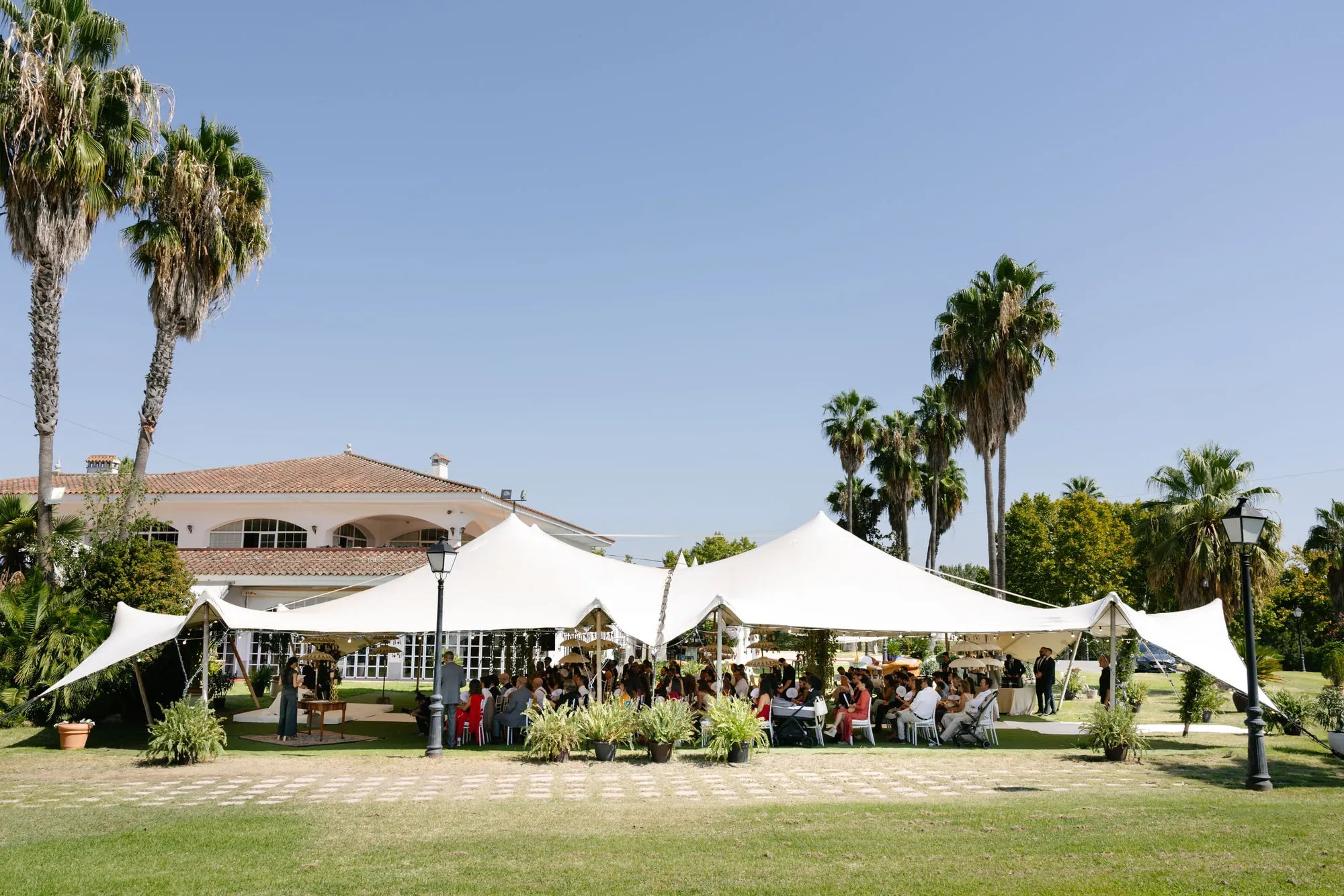 Invitados bajo la carpa abierta del jardín del Golf Guadiana (Badajoz), junto a las palmeras