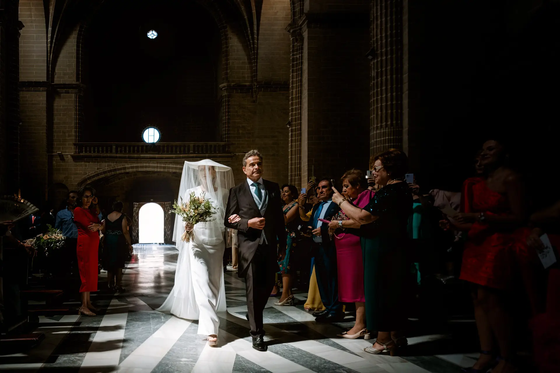 La novia entra en la iglesia del brazo de un familiar entre los invitados