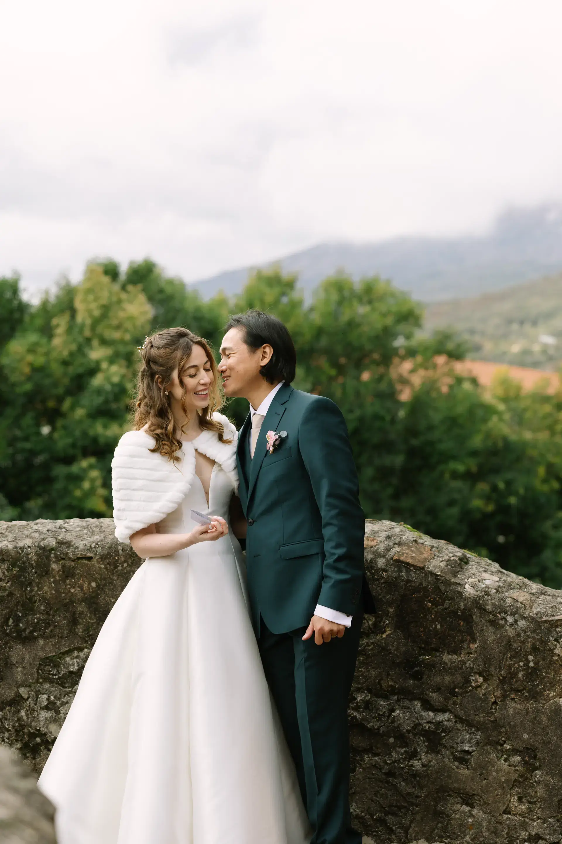 Gemma y Russell abrazados junto a un muro con vistas a la sierra, en el Parador de Jarandilla