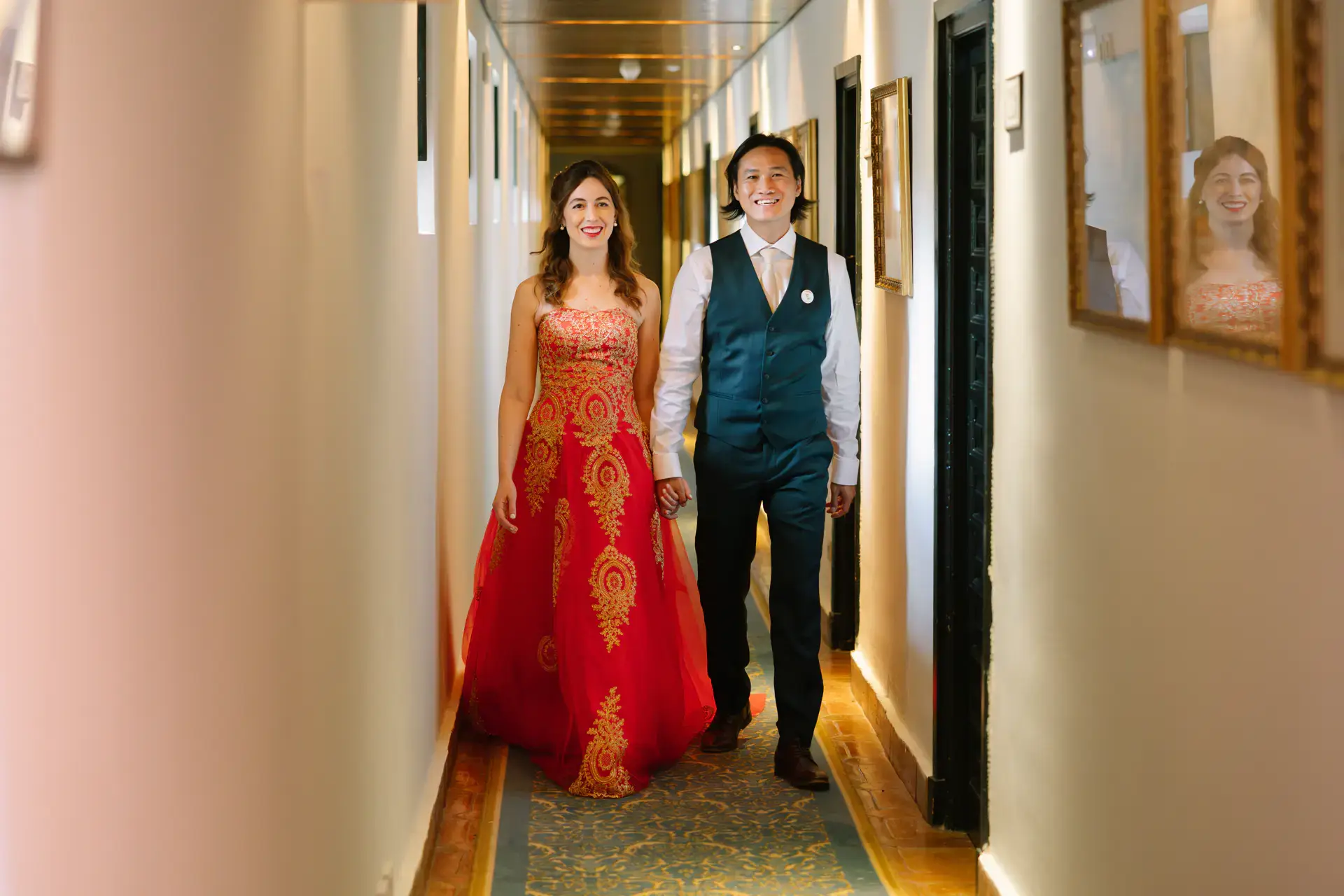Gemma, con su segundo vestido rojo y dorado, camina con Russell por un pasillo, en el Parador de Jarandilla