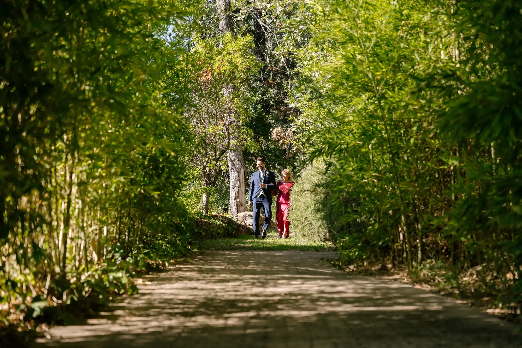 Rubén y una acompañante caminan por un sendero entre árboles hacia la ceremonia, en el Hotel Ruta Imperial de Jarandilla