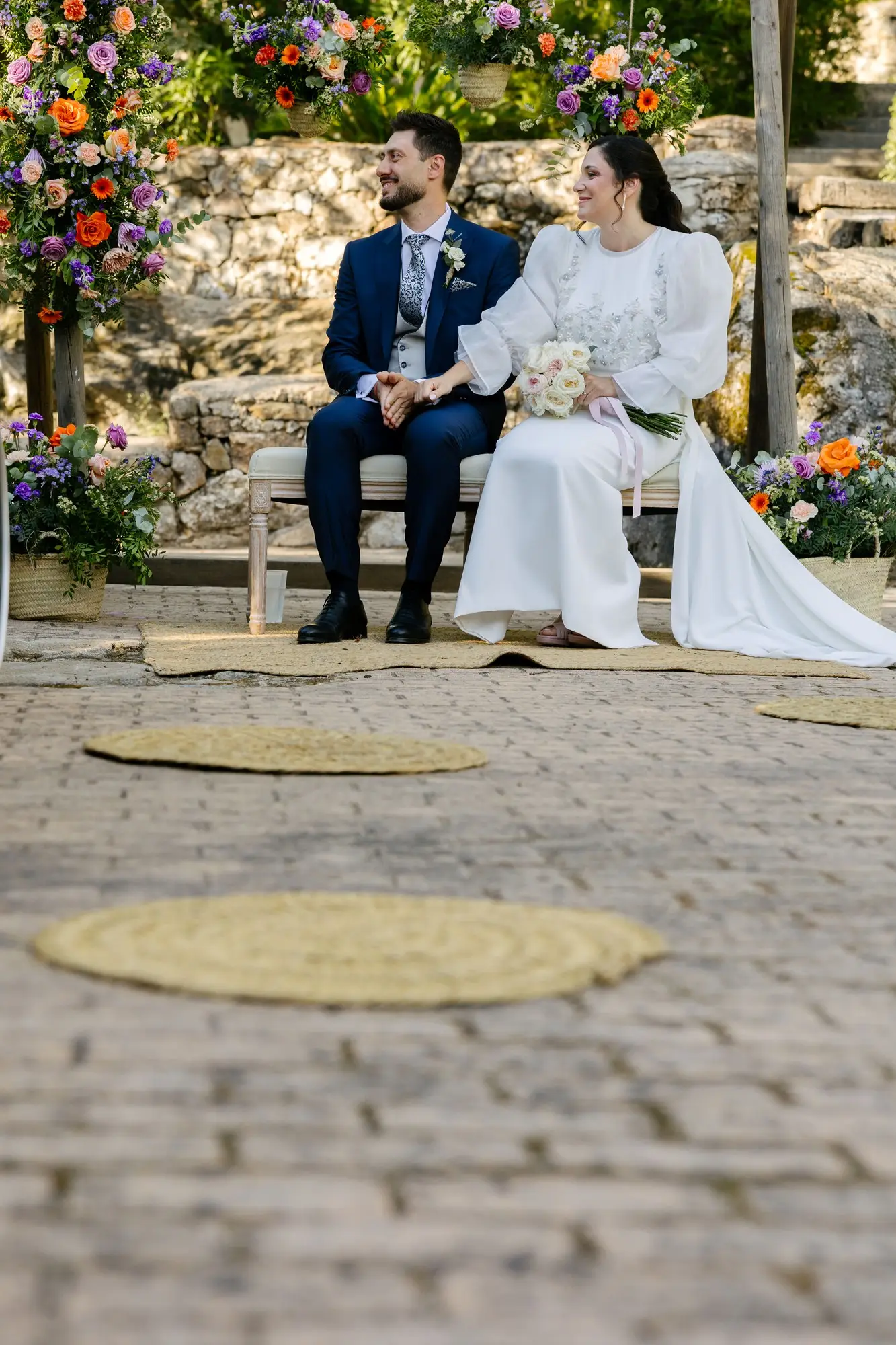 Lara y Rubén en el banco, con alfombras de esparto en el suelo de piedra, en el Hotel Ruta Imperial de Jarandilla