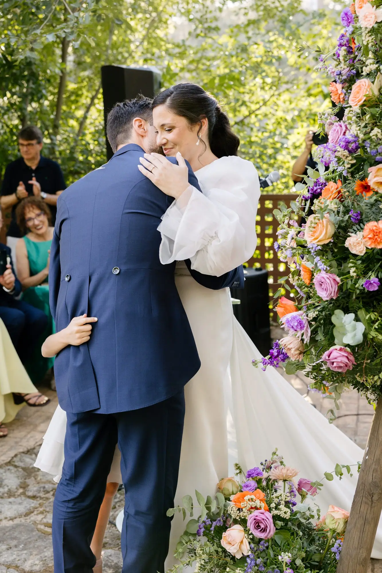 Lara y Rubén se abrazan de pie bajo la pérgola de flores, en el Hotel Ruta Imperial de Jarandilla