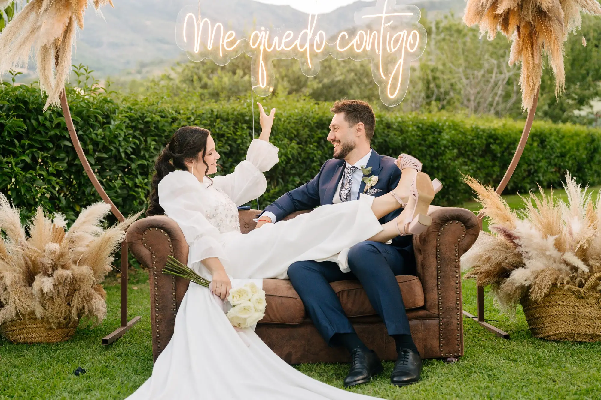 Lara y Rubén en un sofá de cuero bajo el cartel de luces «Me quedo contigo», en el Hotel Ruta Imperial de Jarandilla