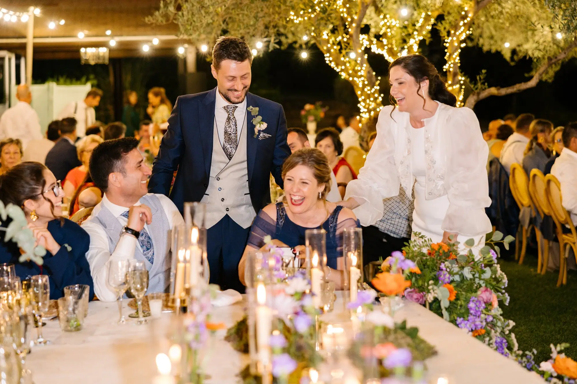 Lara y Rubén de pie en su mesa durante la cena, bajo los árboles con luces, en el Hotel Ruta Imperial de Jarandilla