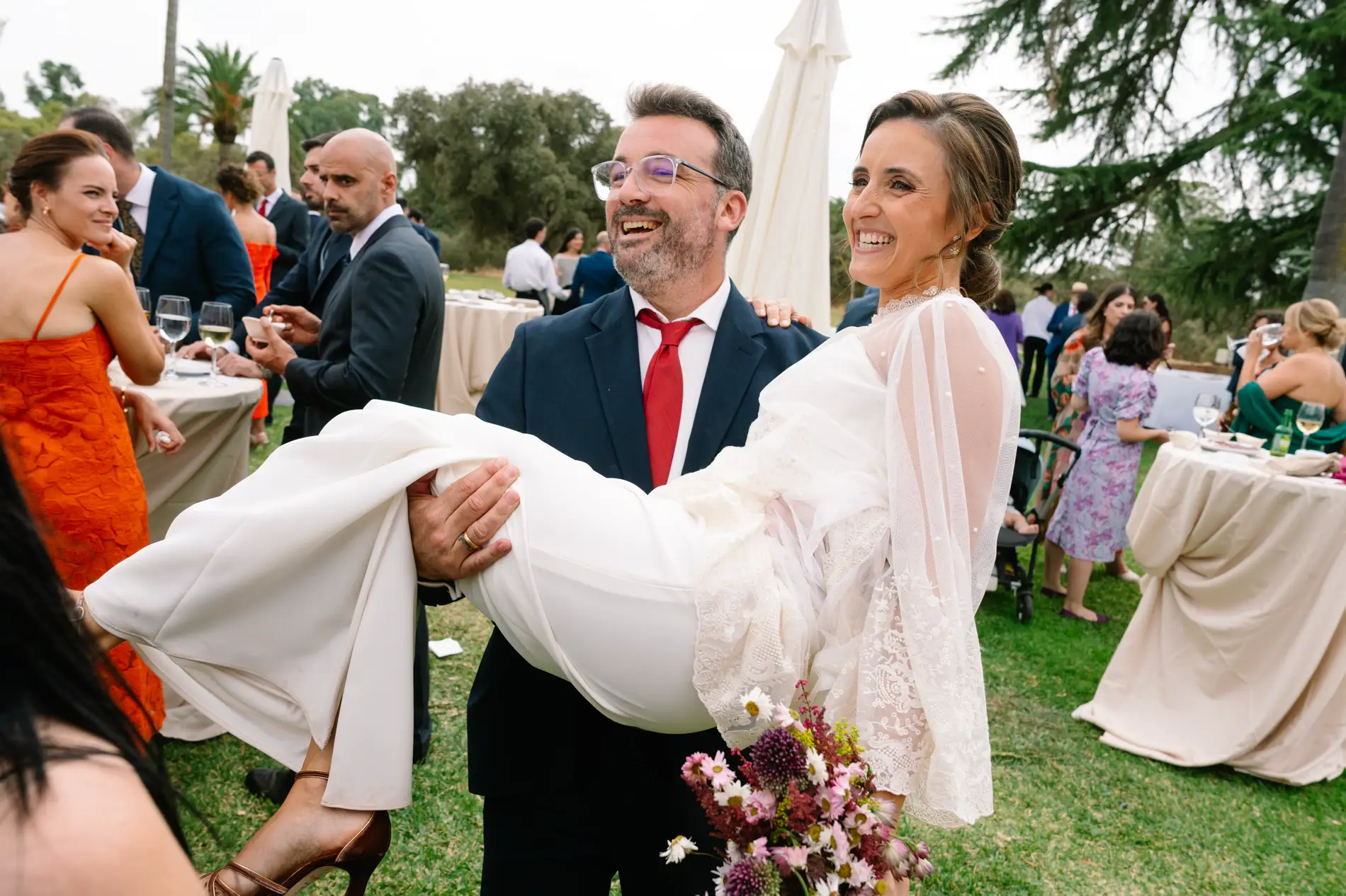 Un invitado levanta en brazos a María en el jardín, en Casa Colorada, Badajoz