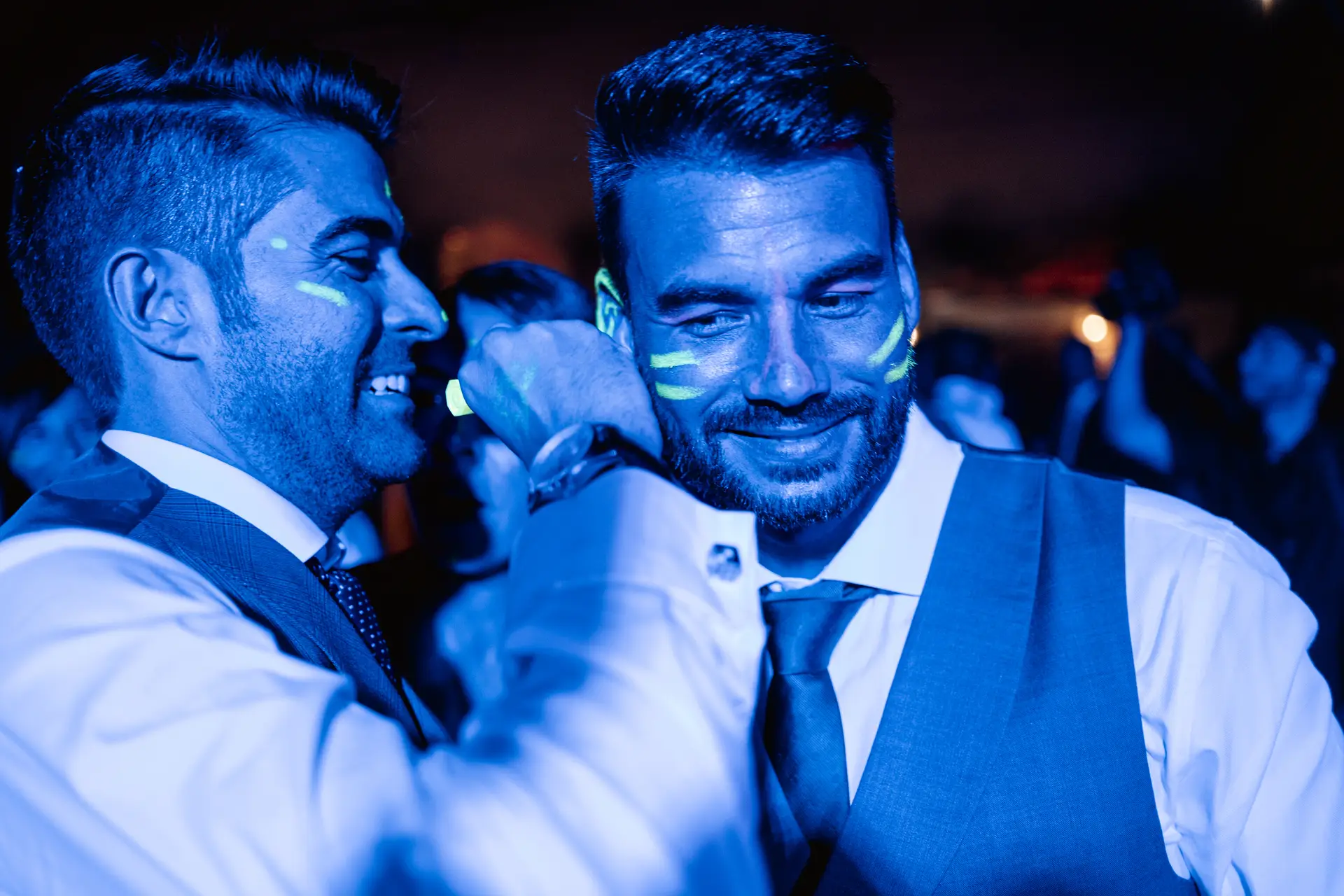 Dos amigos con pintura fluorescente en la cara bajo luz azul, en Mérida