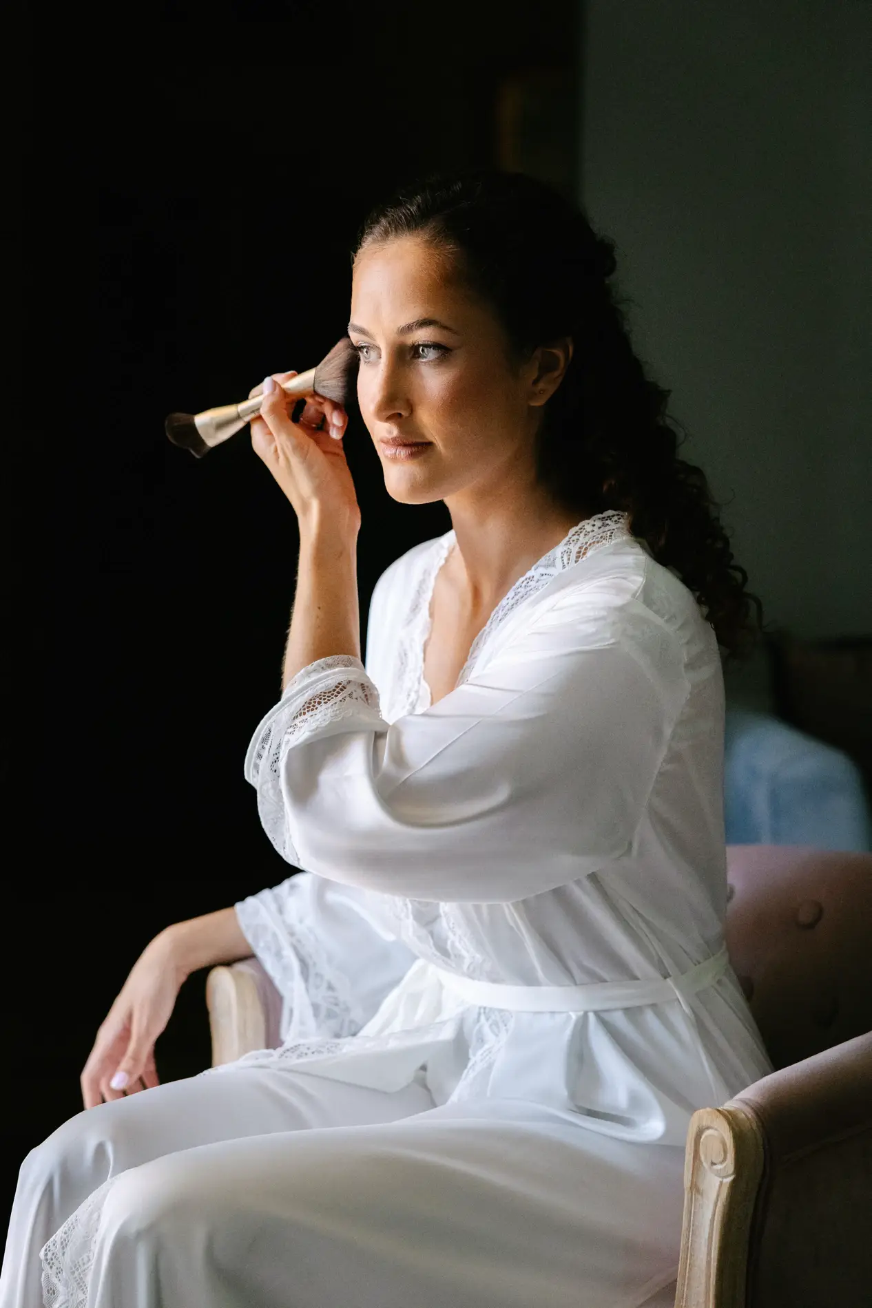 Natalia, en bata blanca, retoca su maquillaje junto a la ventana, en Badajoz