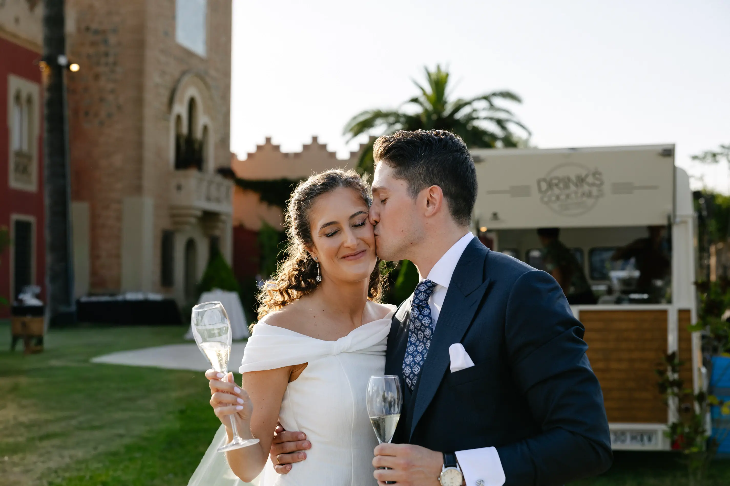 Beso de los novios con copas de cava en el jardín de Casa Colorada