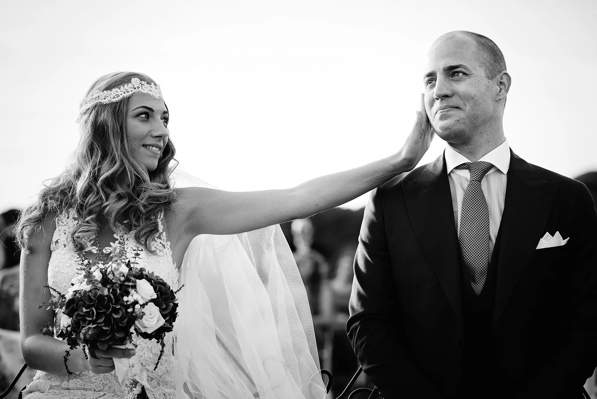 La novia, con diadema de encaje y ramo, acaricia la cara del novio durante la ceremonia, en blanco y negro