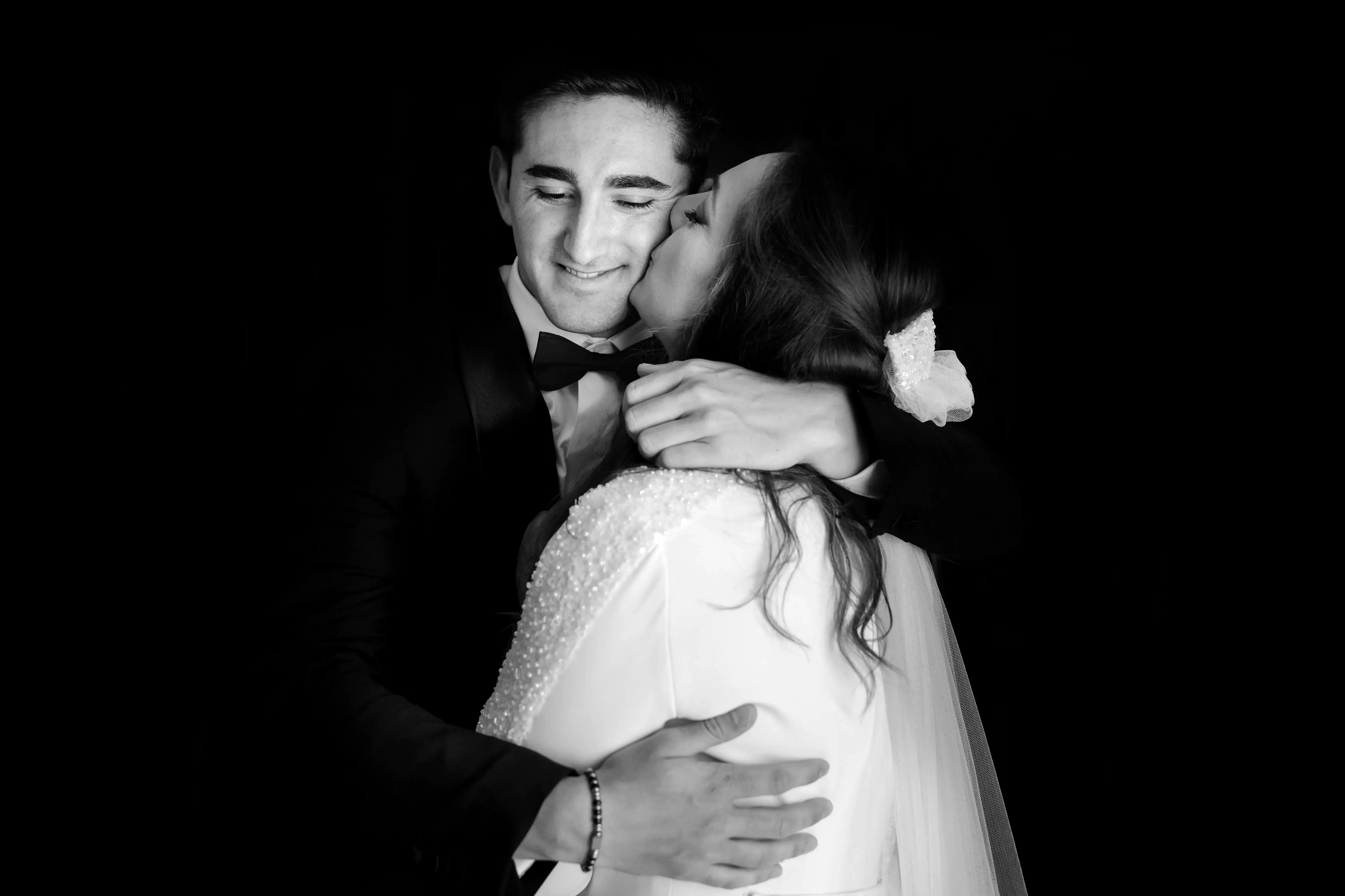 La novia besa al novio en la mejilla, en blanco y negro