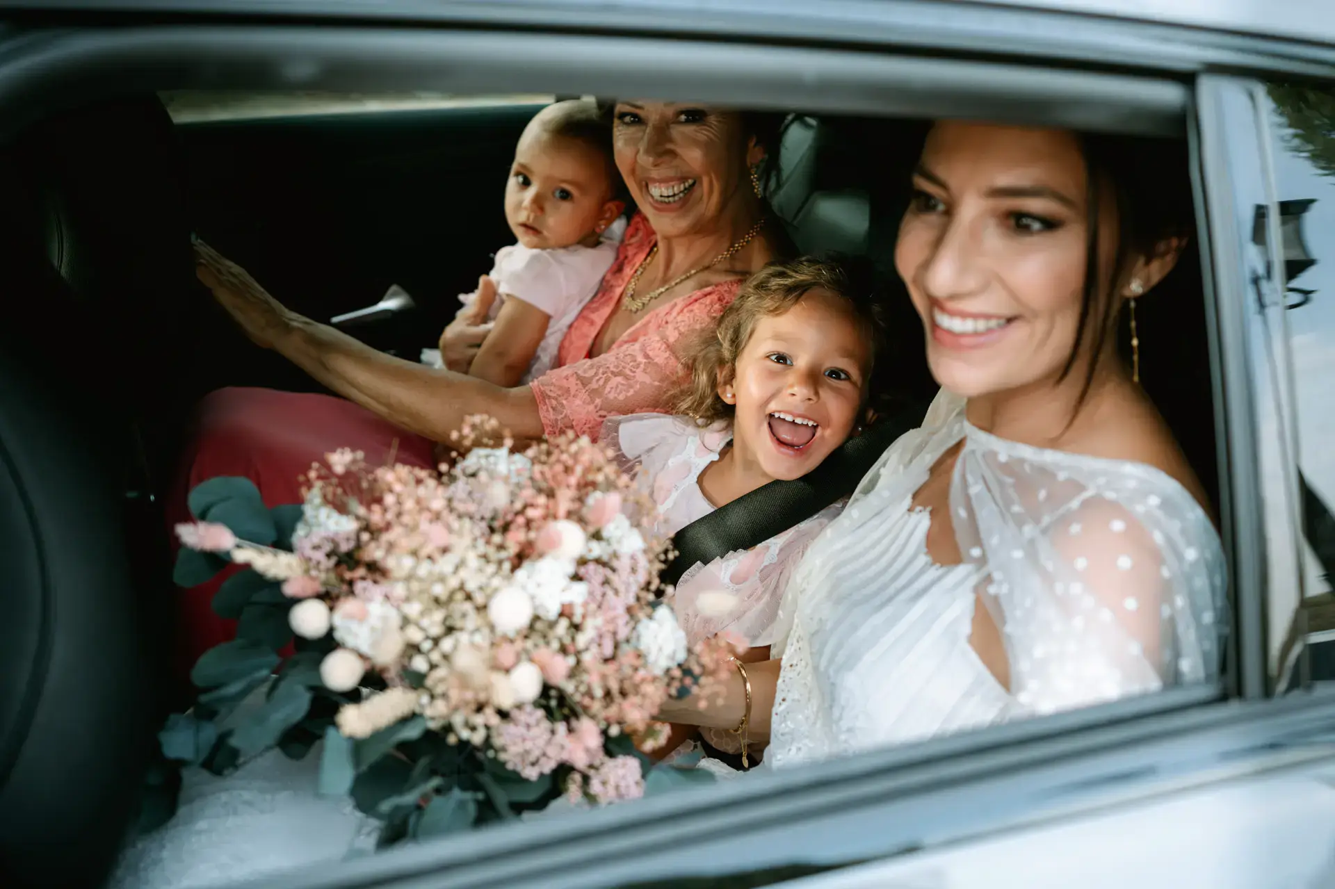 La novia ríe en el coche con dos niñas y una familiar