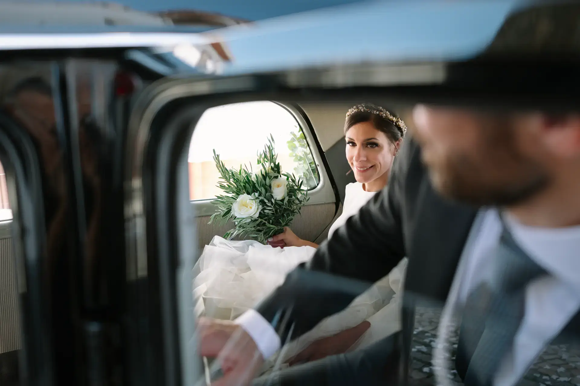 La novia sonríe desde el coche mientras el novio abre la puerta