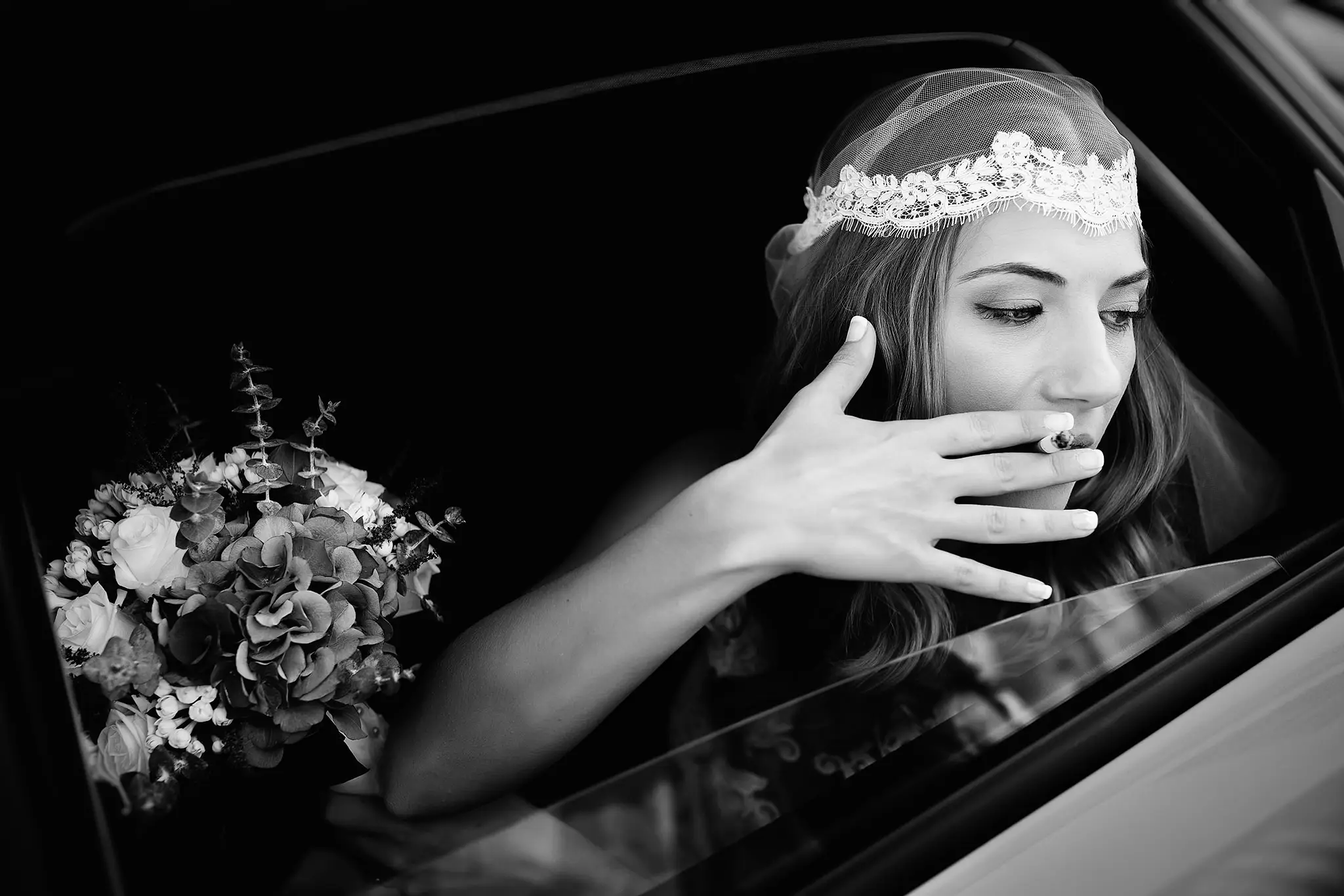 La novia, con velo corto y ramo, se asoma por la ventanilla del coche, en blanco y negro