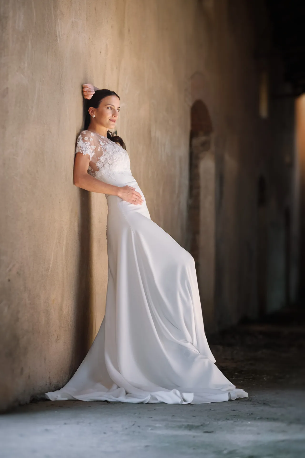 Novia apoyada en un muro con su vestido de cola