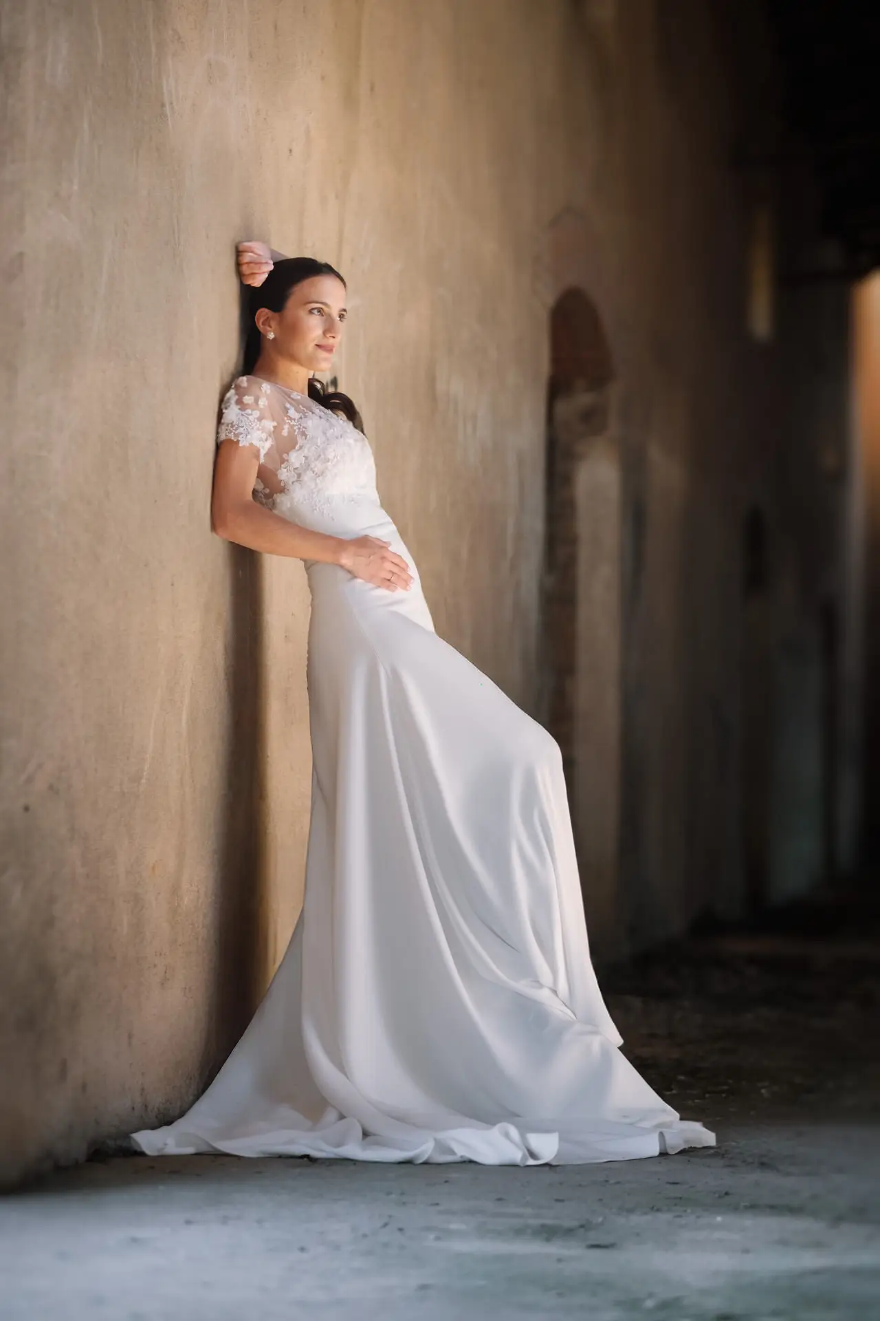 Novia apoyada en un muro con su vestido de cola
