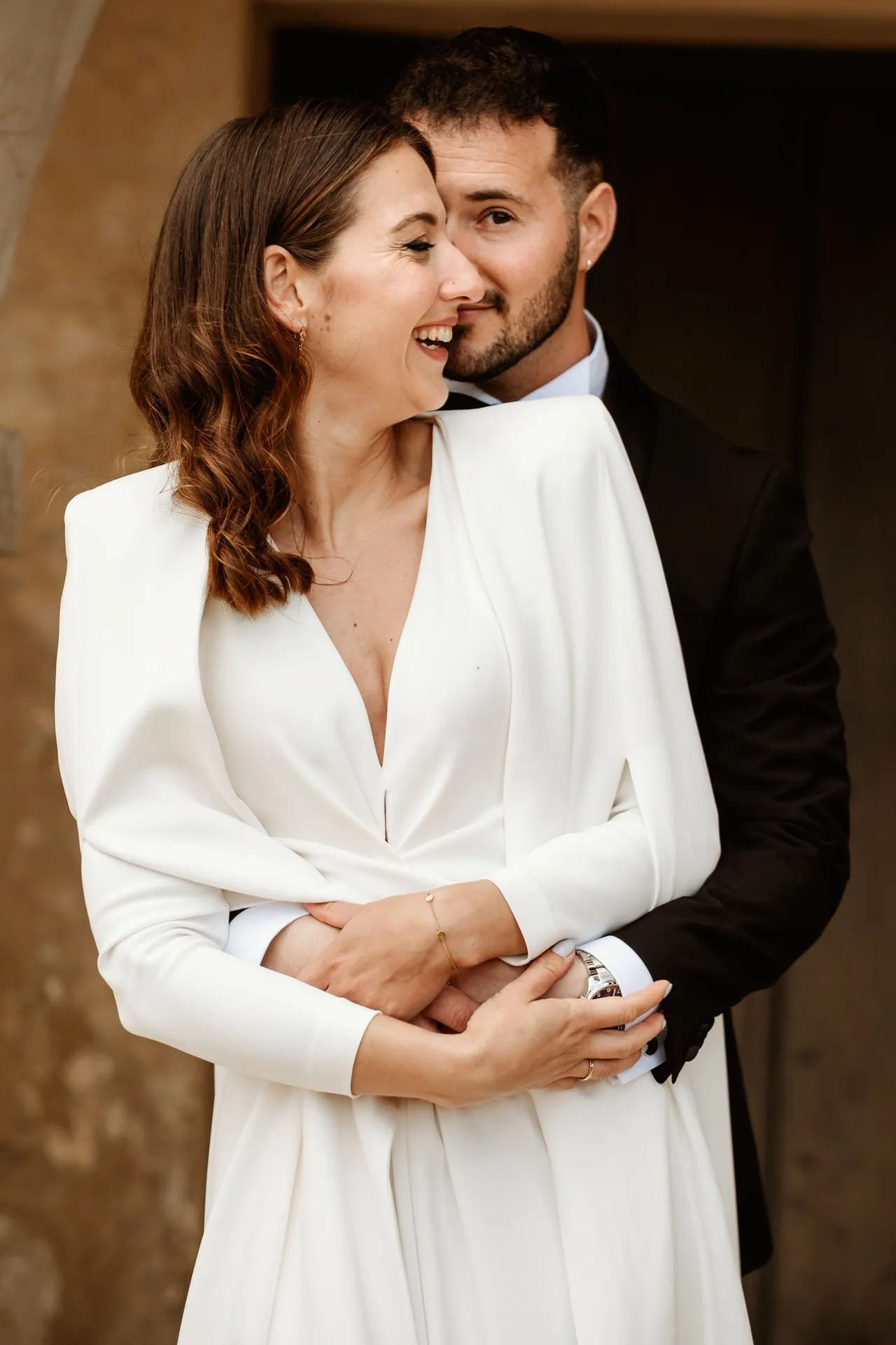 El novio abraza a la novia por la espalda junto a una puerta