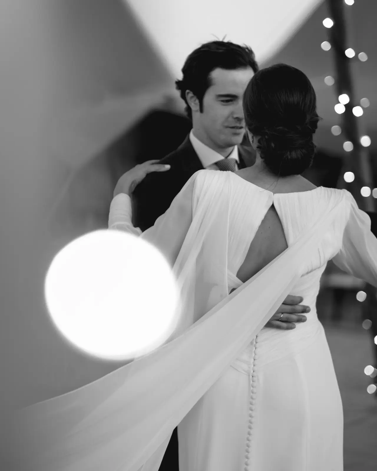 El novio mira a la novia de espaldas con su capa, en blanco y negro