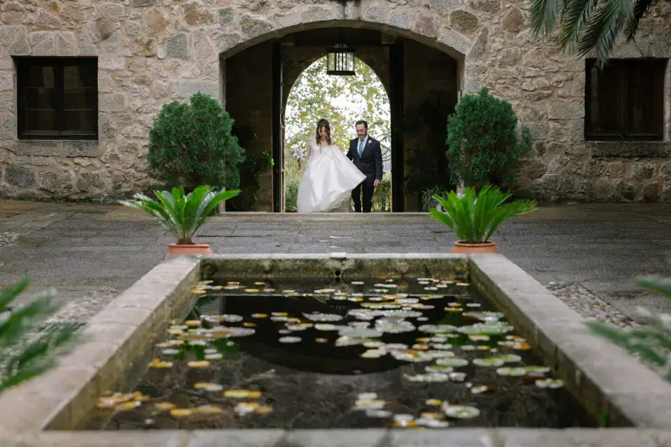 Los novios bajo un arco de piedra junto a un estanque con nenúfares