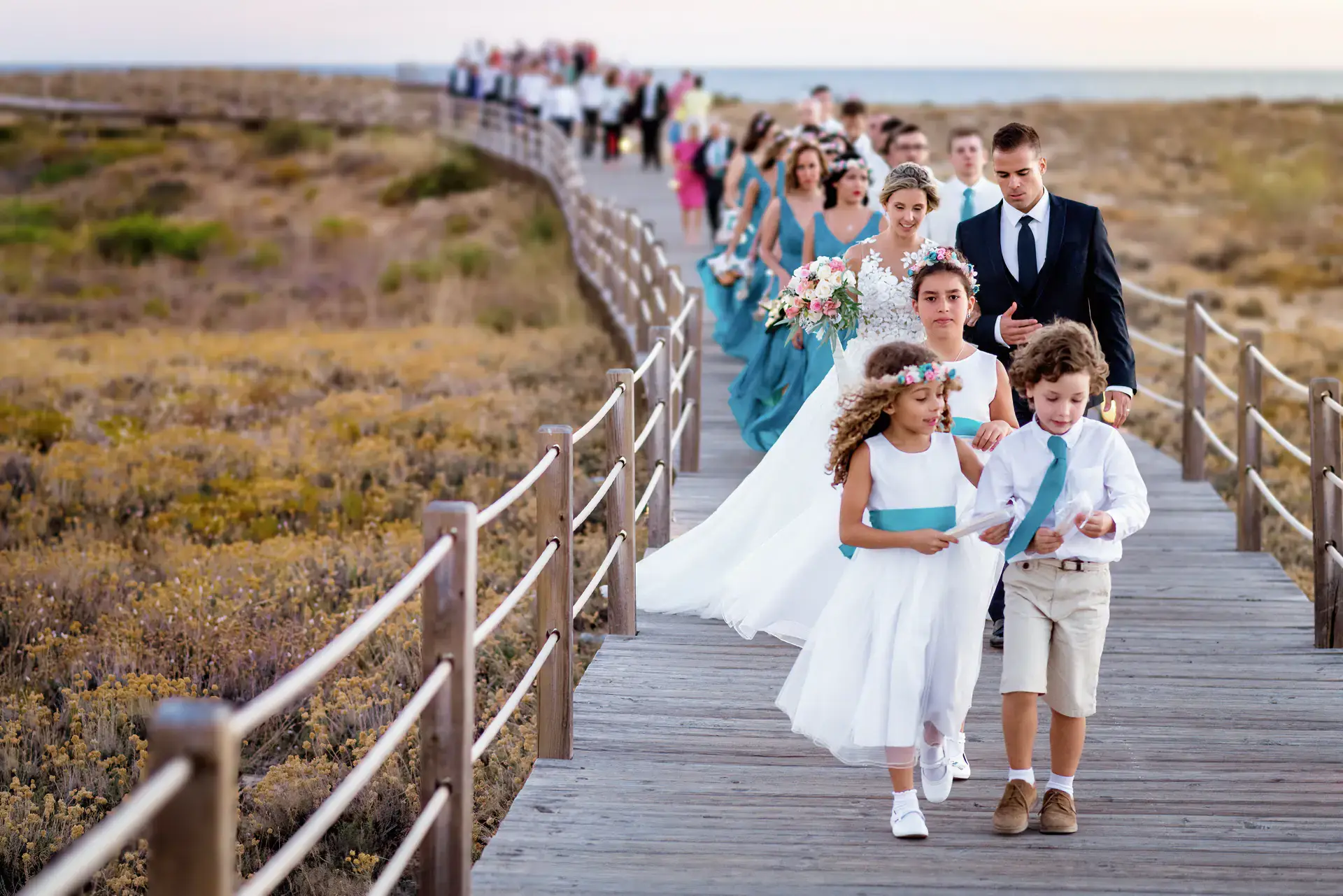 Cortejo de boda con niños por una pasarela de madera junto al mar