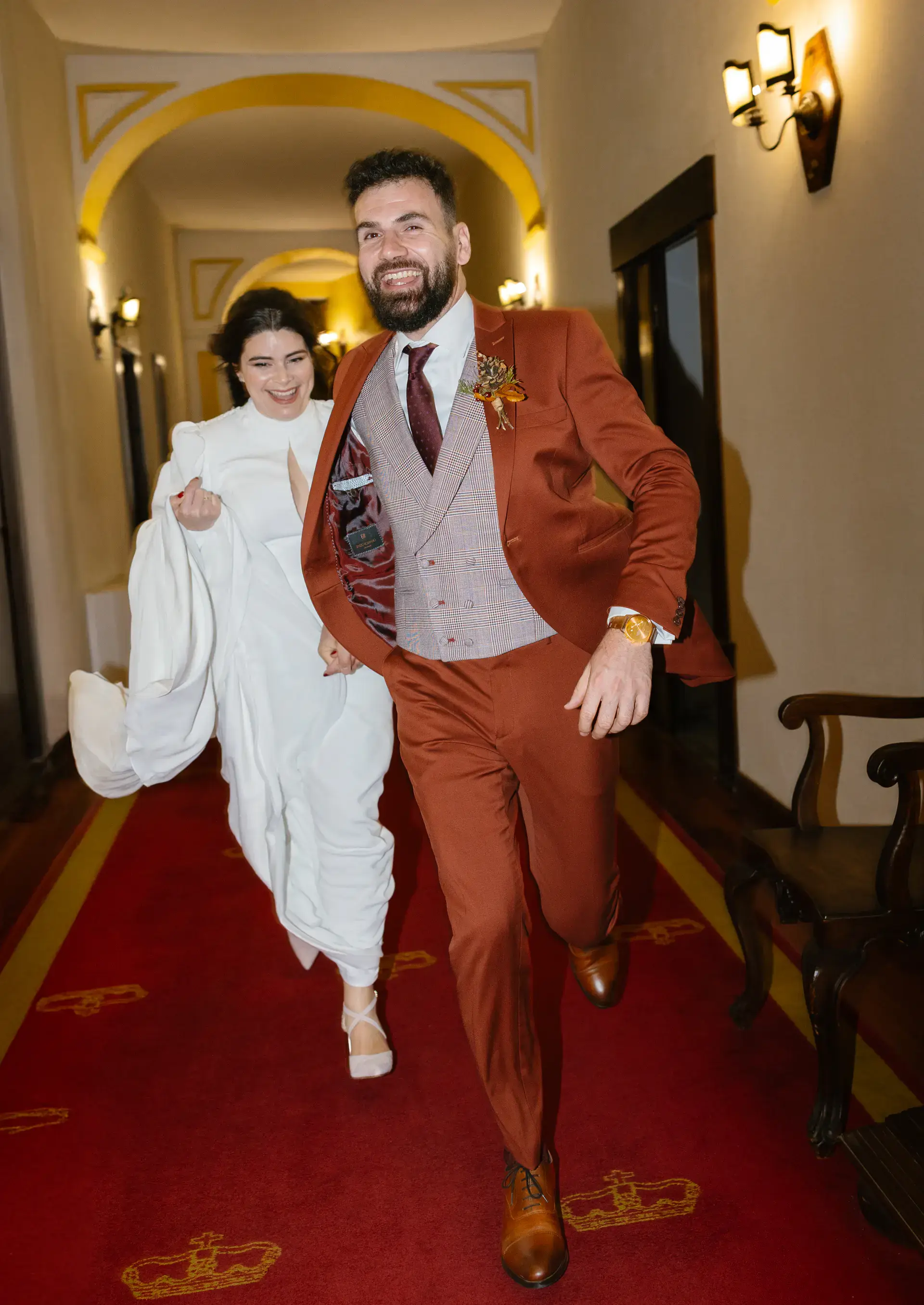 Los novios corren riendo por un pasillo con alfombra roja