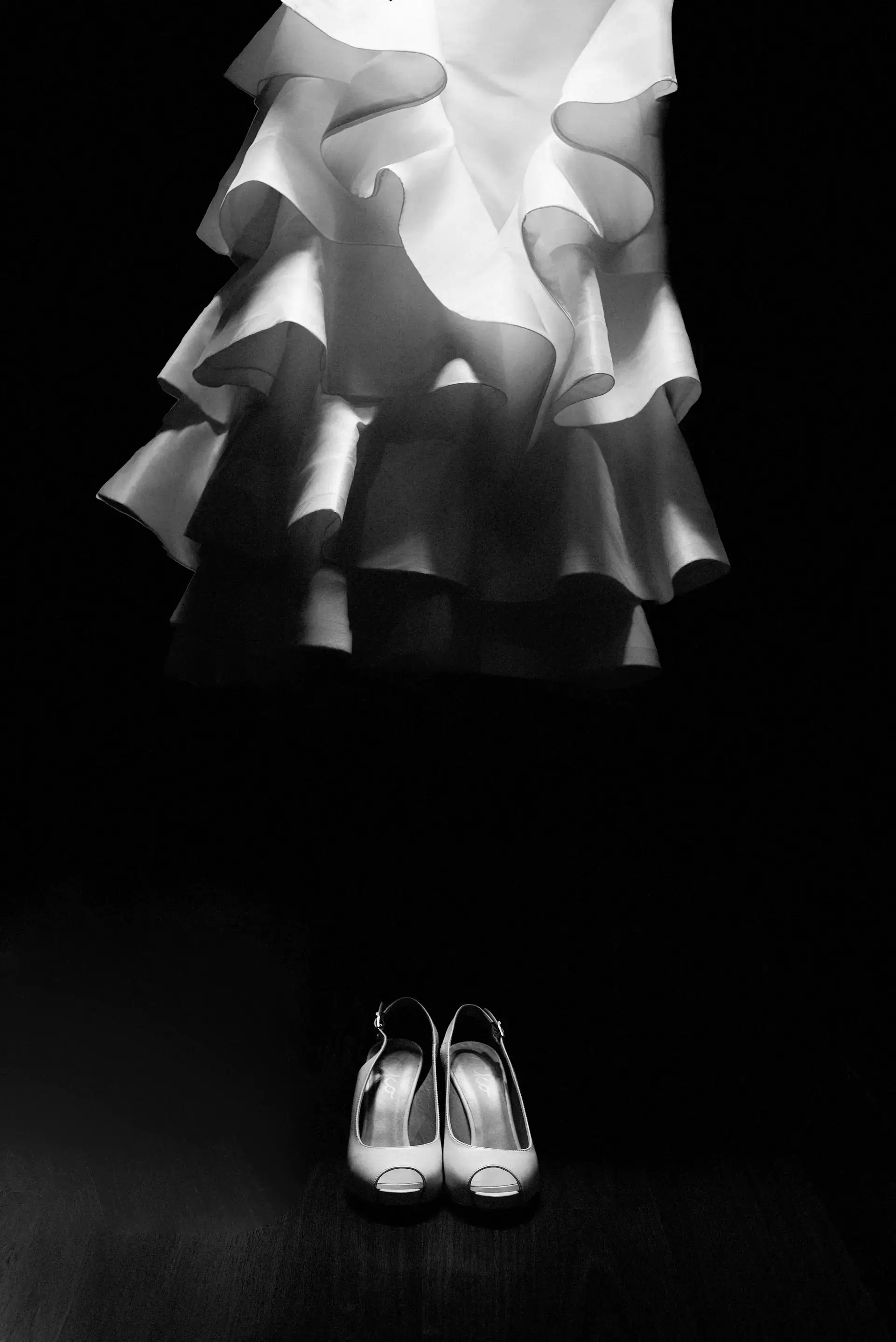 Vestido de novia colgado sobre los zapatos de novia, en blanco y negro