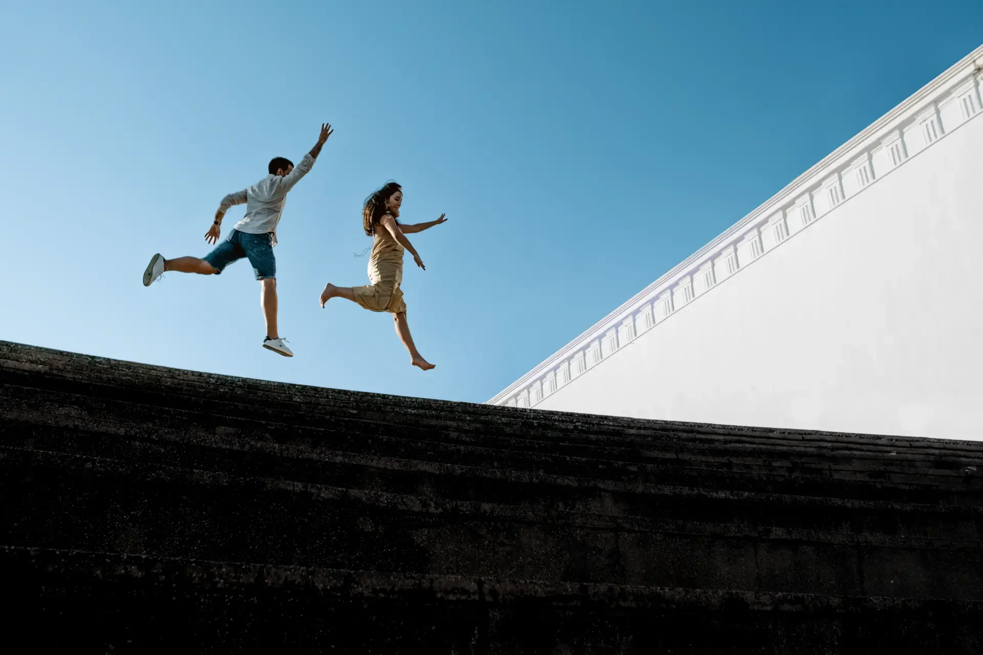 Los novios saltan sobre un muro blanco con el cielo azul detrás