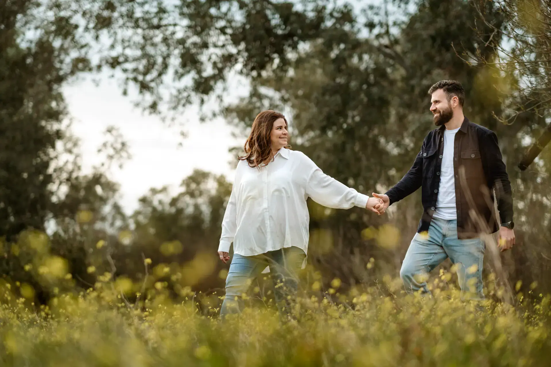 Pareja de la mano en un campo de flores en su sesión de embarazo