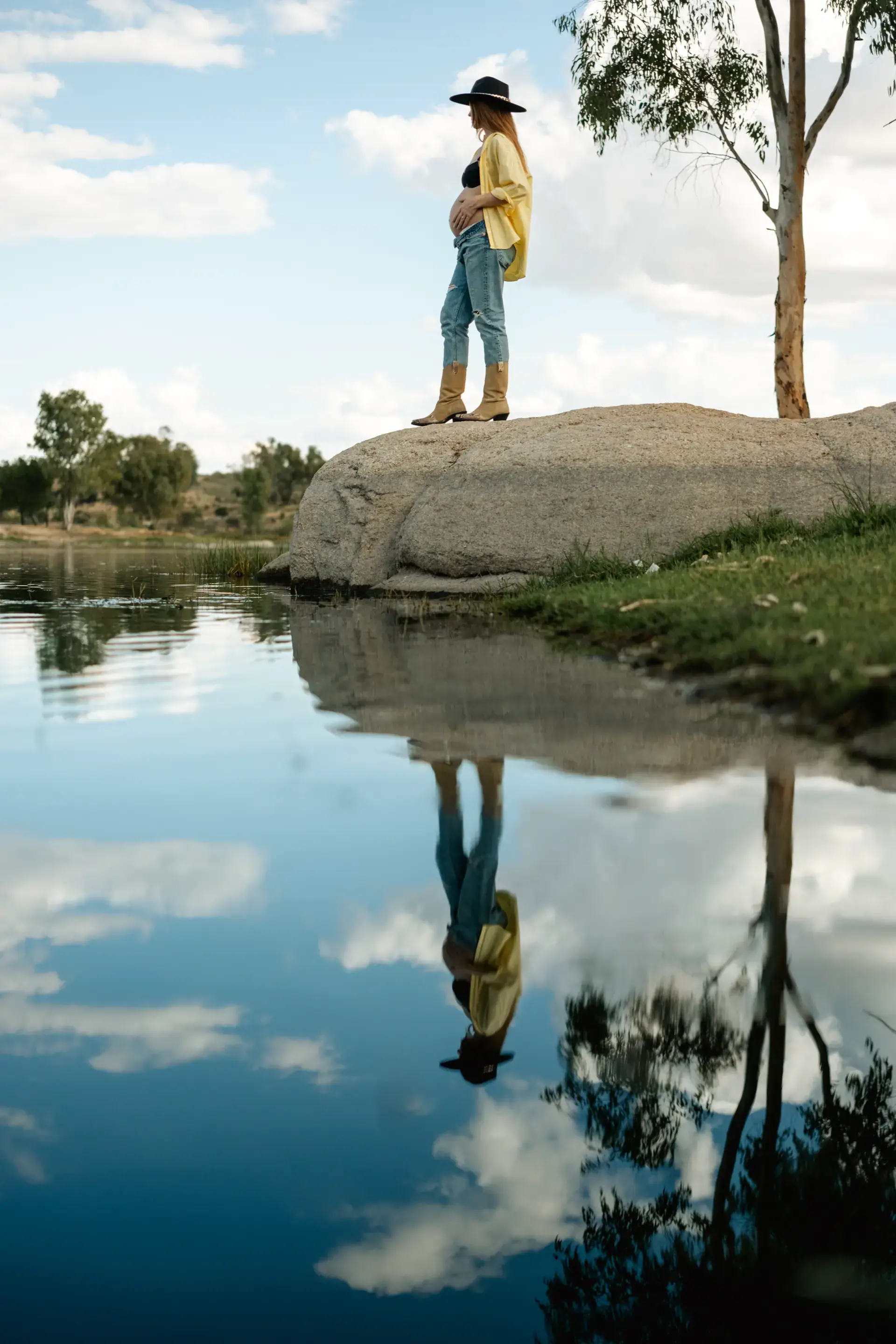 Mujer embarazada sobre una roca reflejada en el agua de un lago