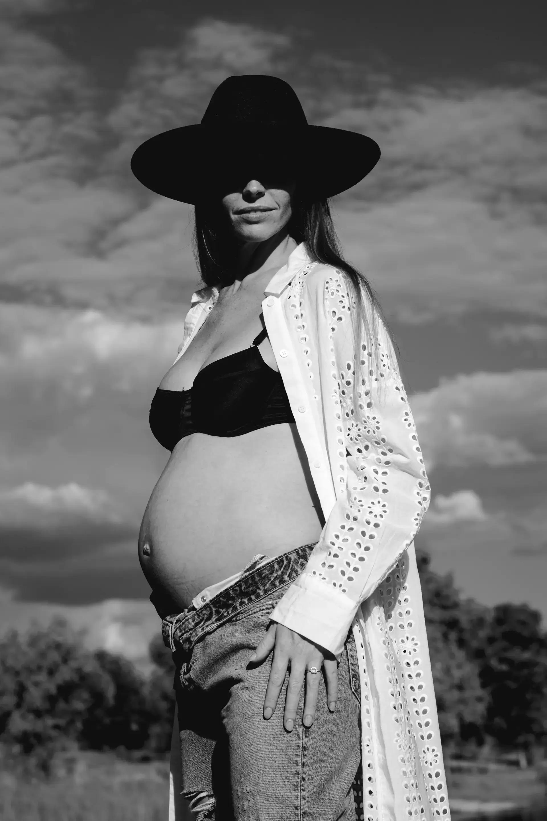 Mujer embarazada con sombrero y camisa calada, en blanco y negro