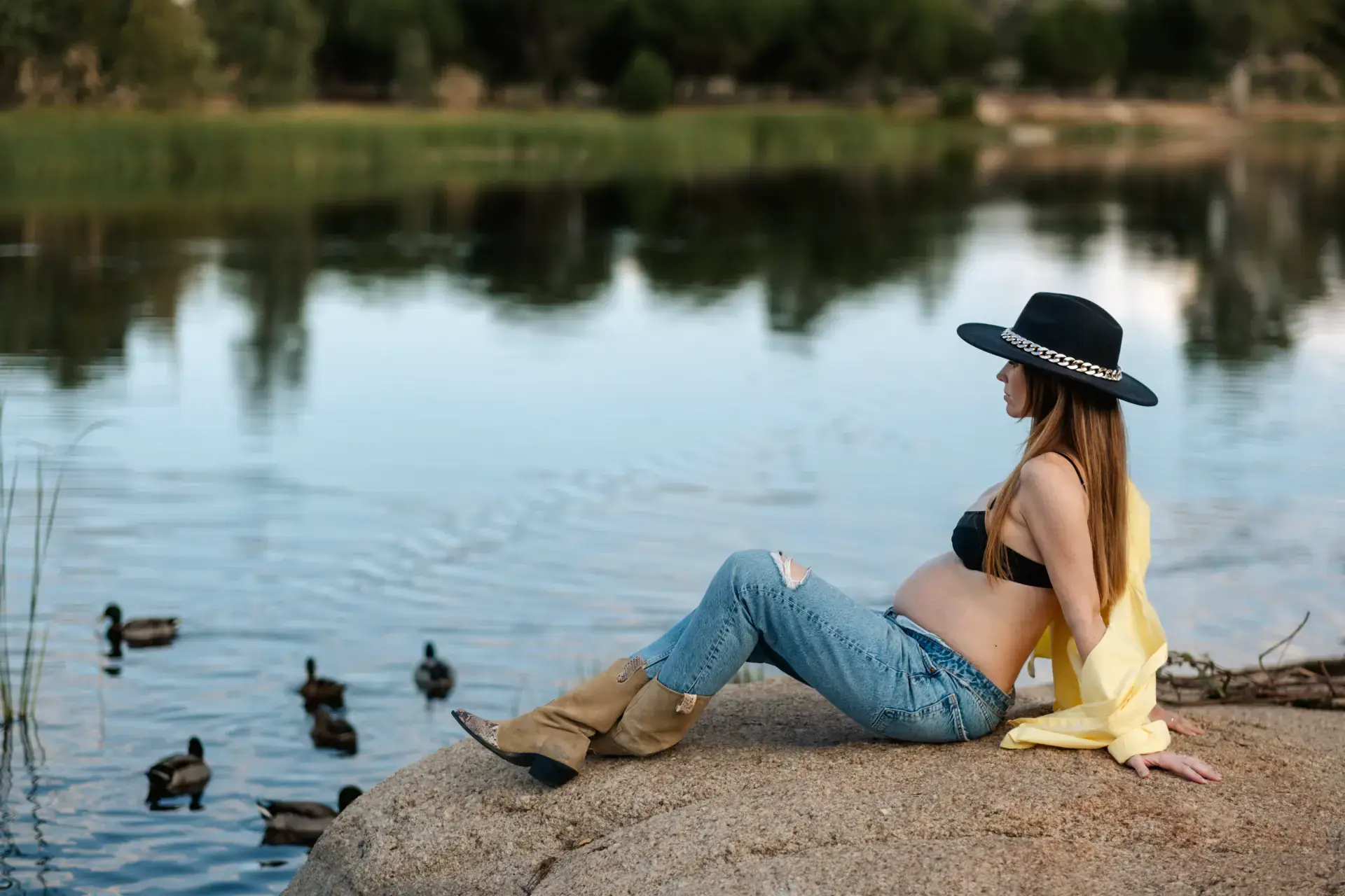 Mujer embarazada sentada en una roca junto al lago con patos