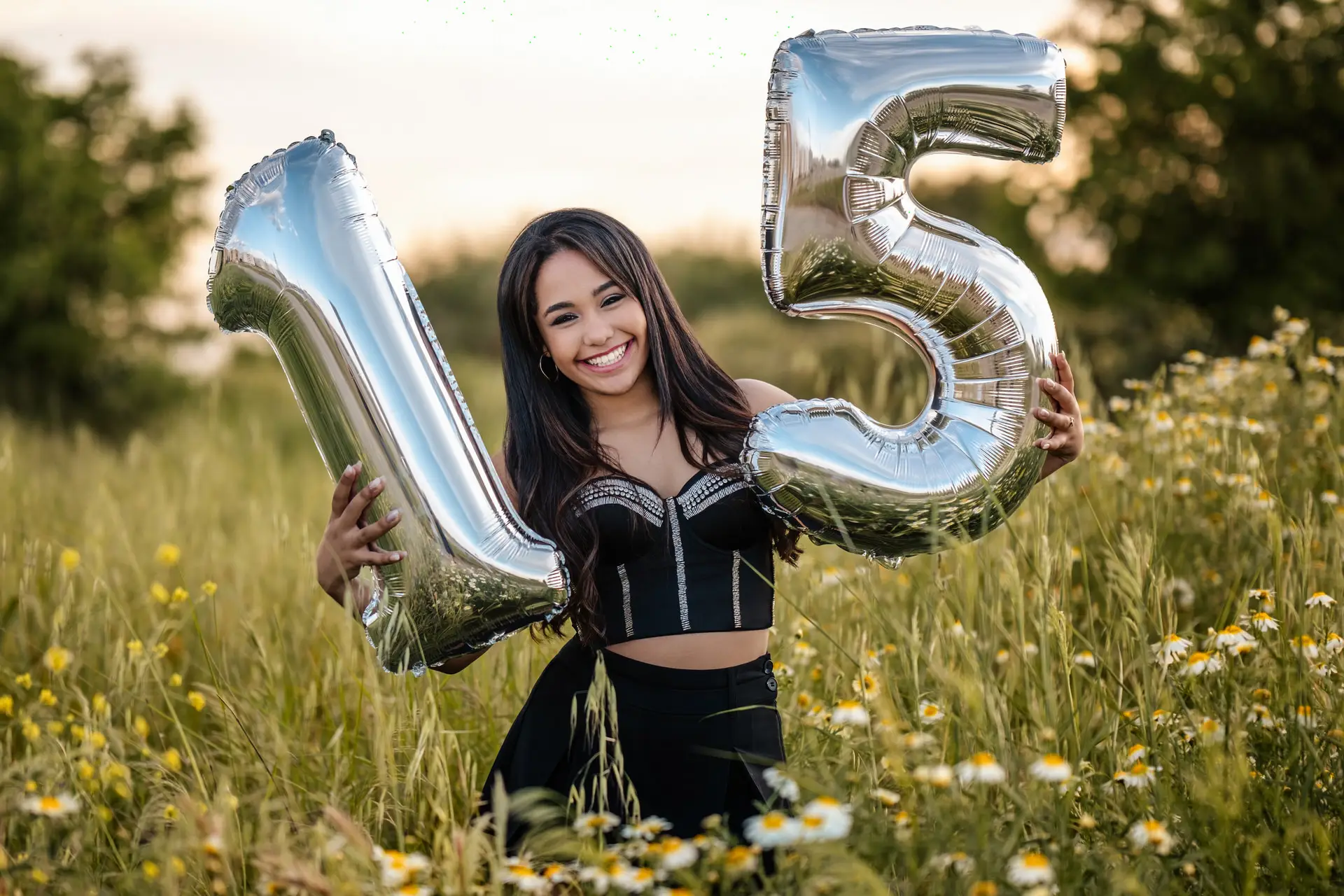 Quinceañera con globos plateados del número 15 en un campo de flores