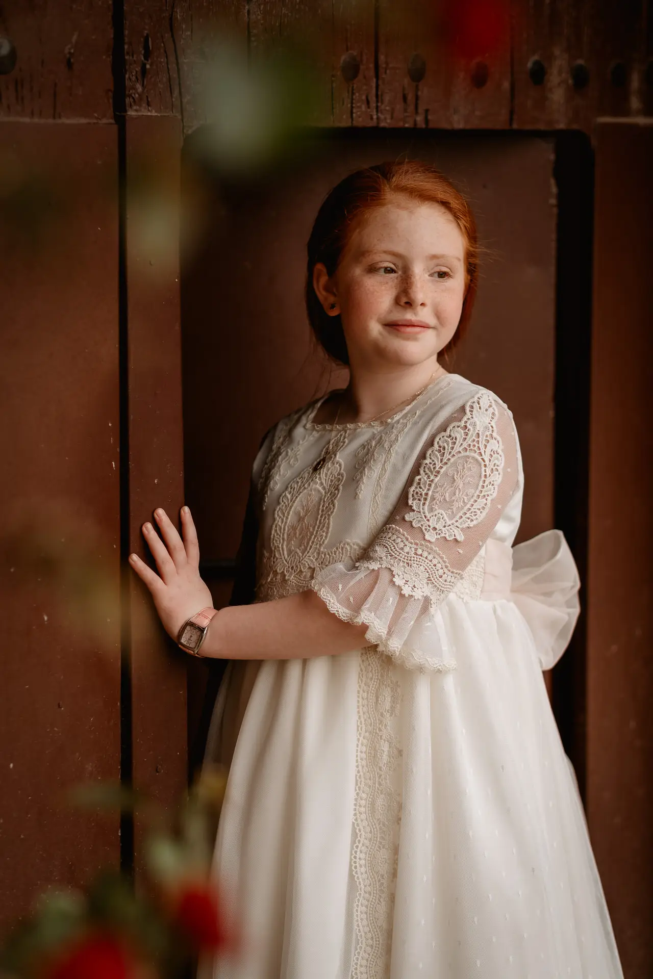 Niña pelirroja con vestido de comunión apoyada en una puerta