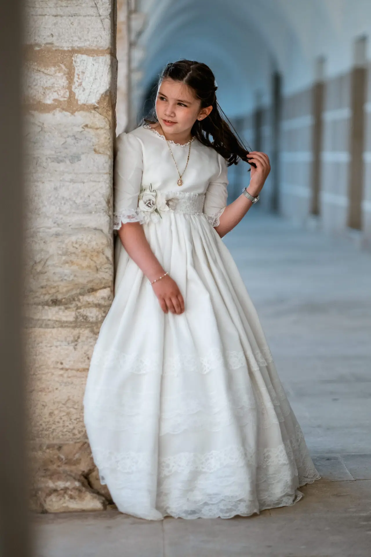 Niña con vestido de comunión bajo unos soportales de piedra