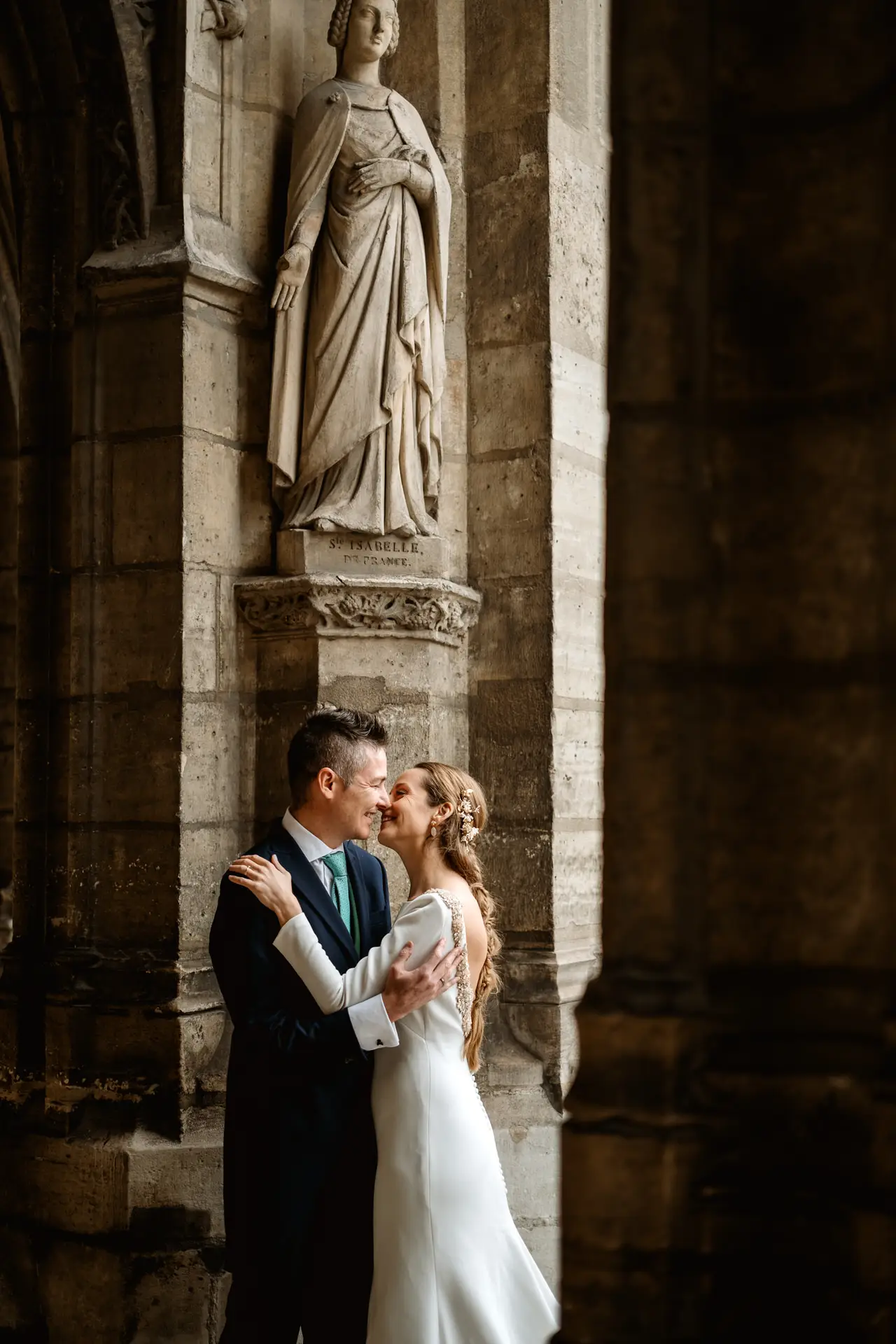 Los novios abrazados junto a la estatua de un pórtico gótico en París