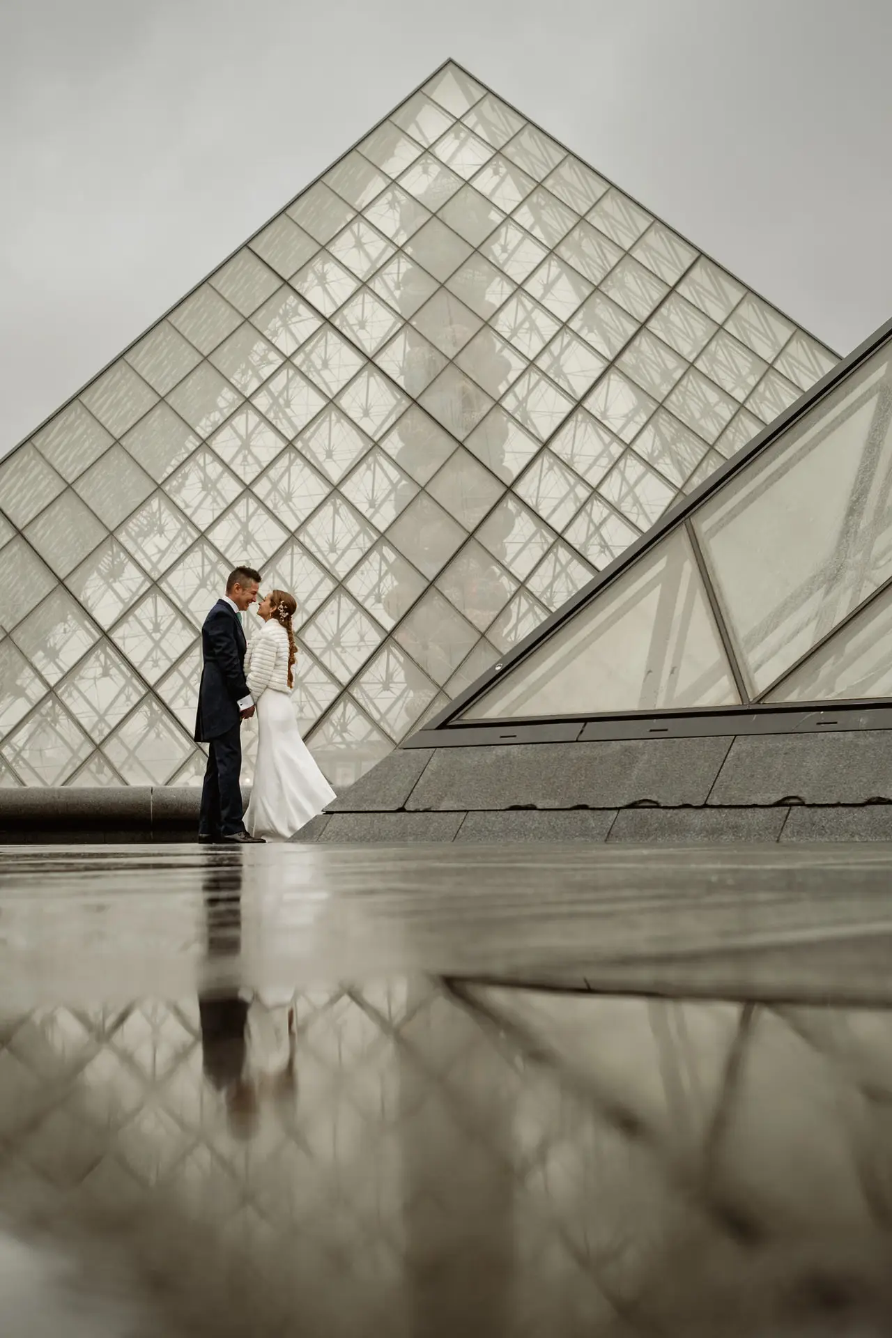 Los novios se besan junto a la pirámide del Louvre reflejada en el suelo