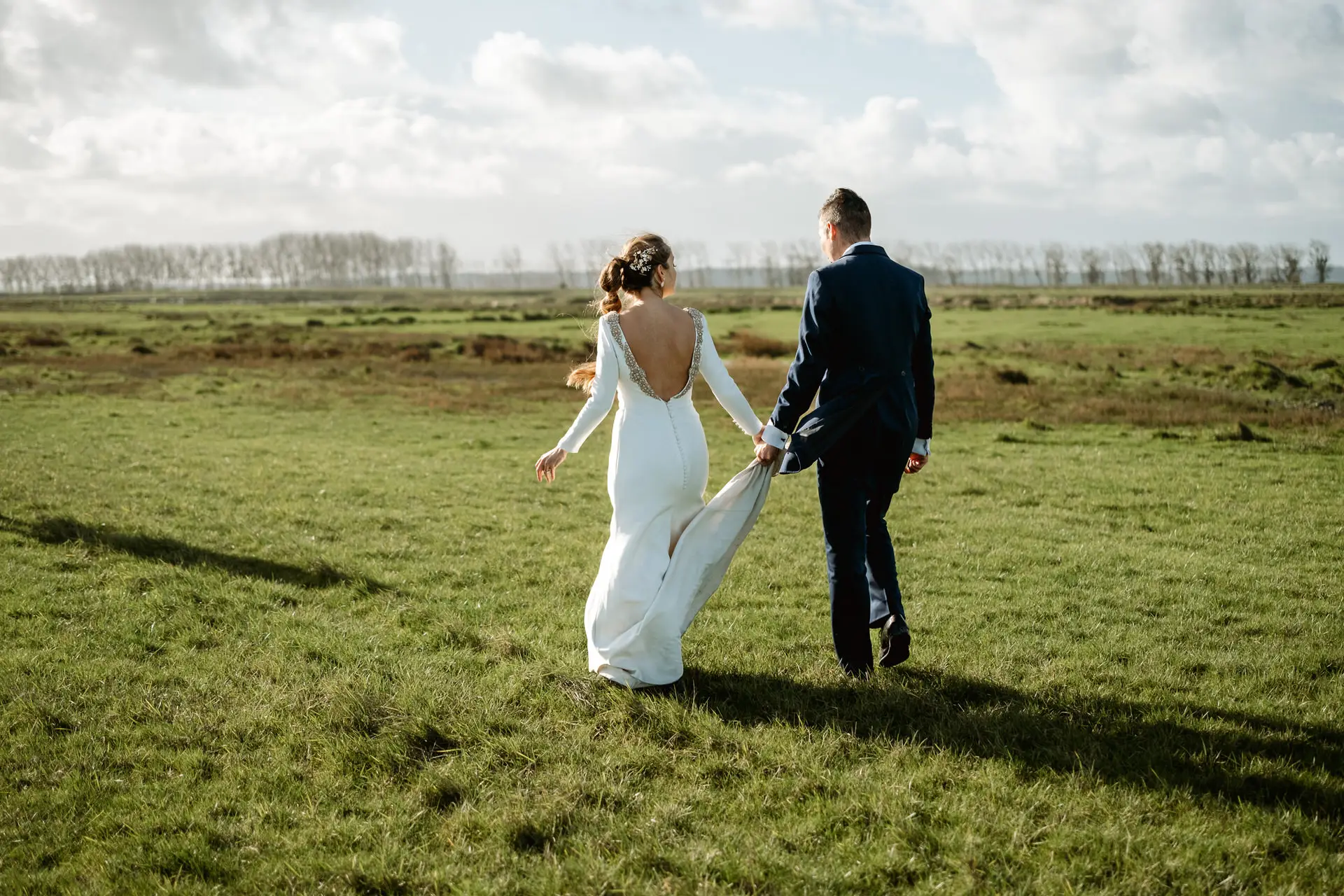 Los novios pasean de la mano por un prado de Normandía