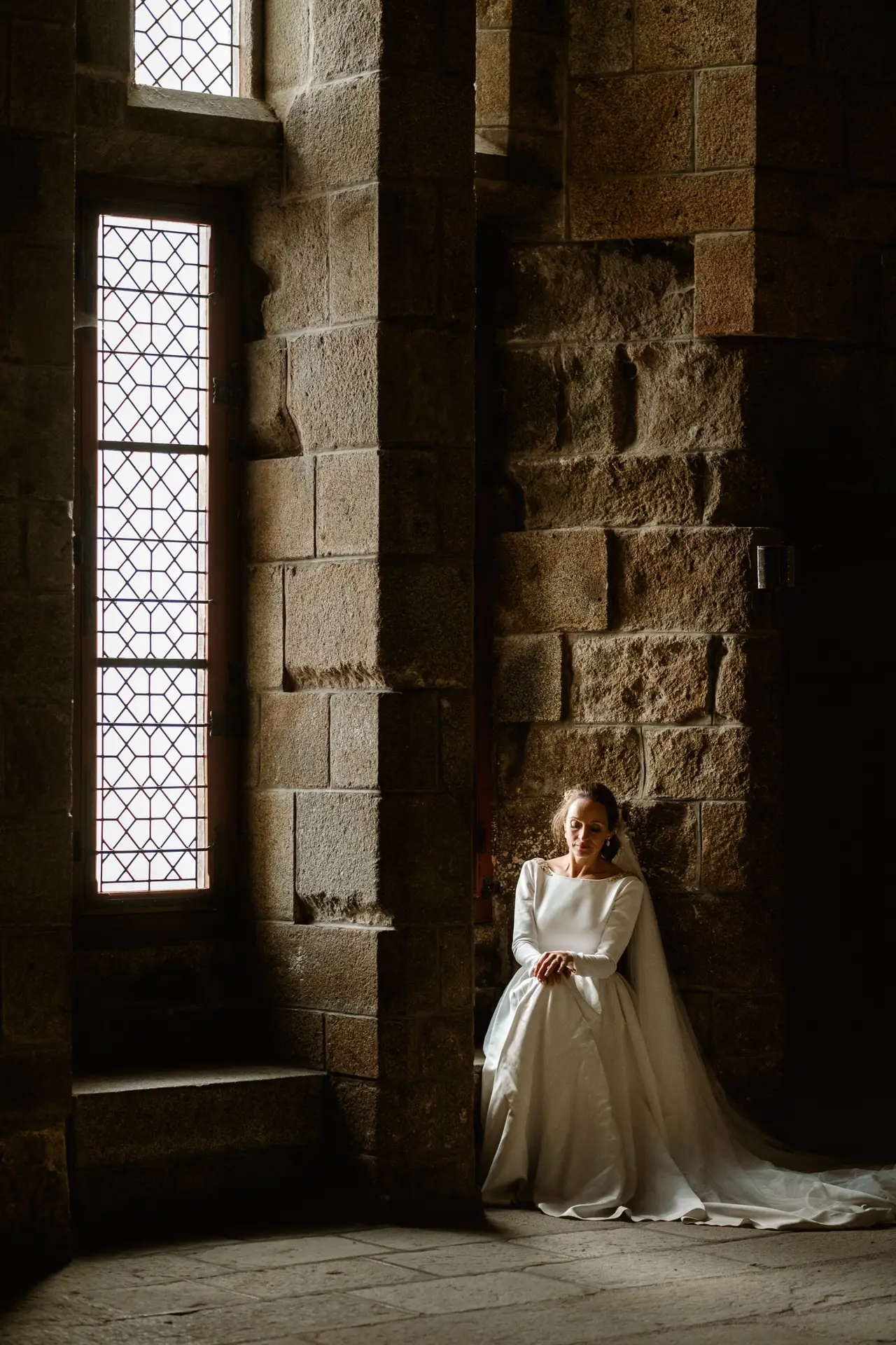 La novia sentada junto a una ventana de la abadía, en su postboda en Francia