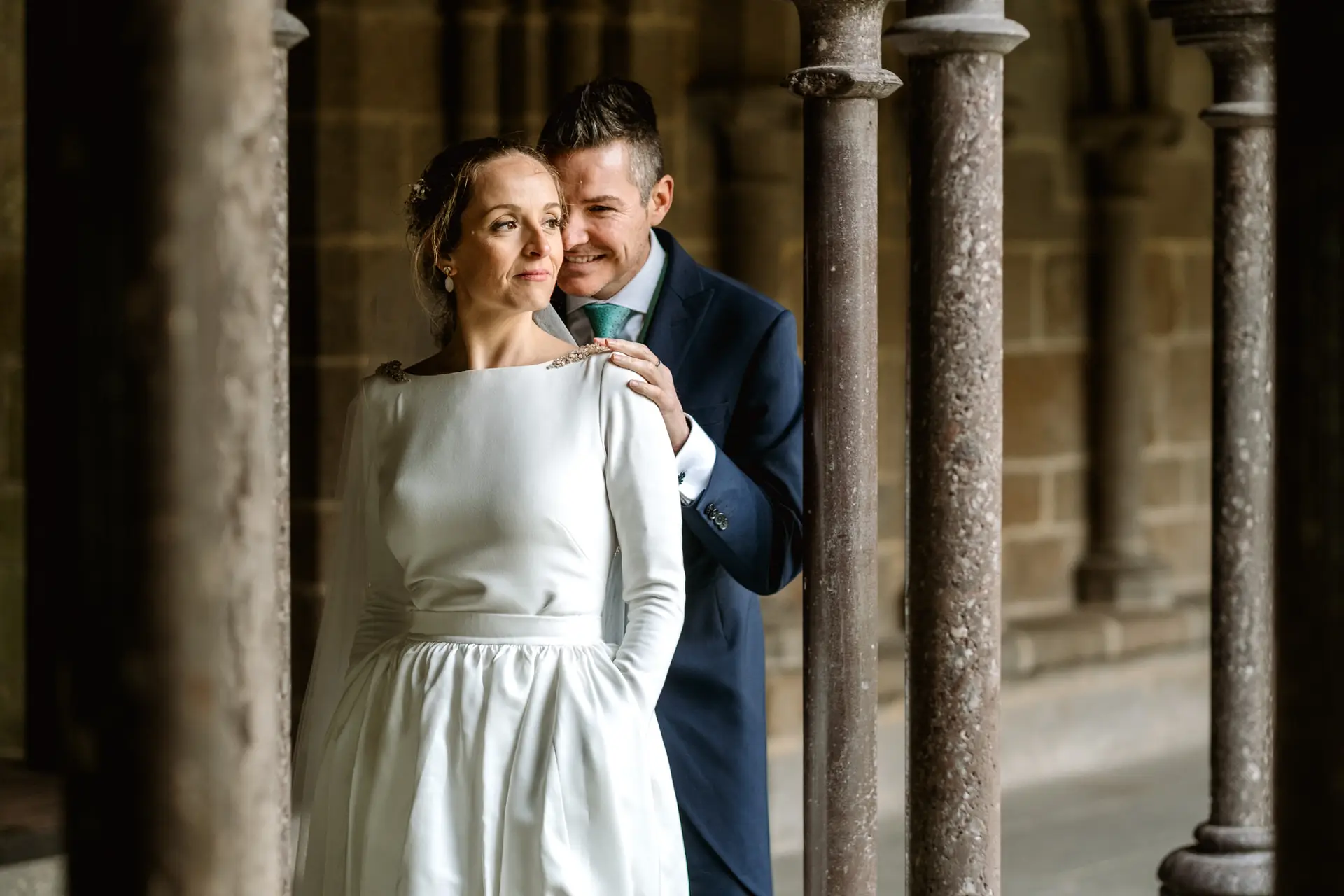 El novio abraza a la novia entre las columnas del claustro, en su postboda en Francia