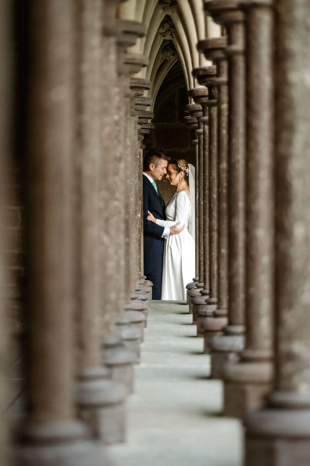 Los novios abrazados al fondo de una fila de columnas, en su postboda en Francia